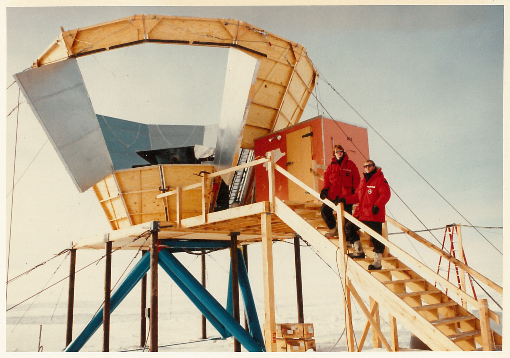 Two people in red parkas standing on an outdoor staircase leading to a cone-shaped structure.