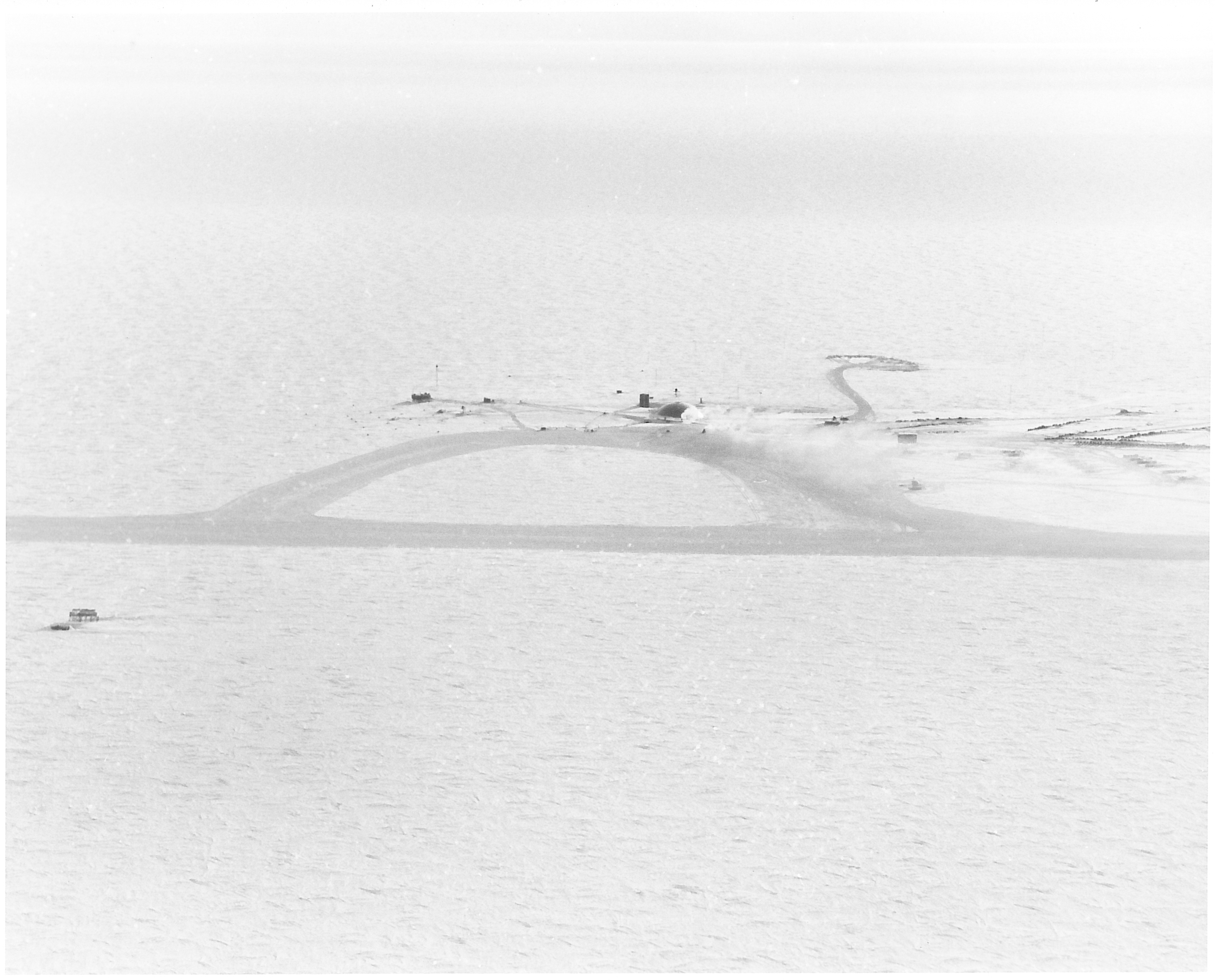 An aerial view of a snow-covered landscape. Structures in the distance.