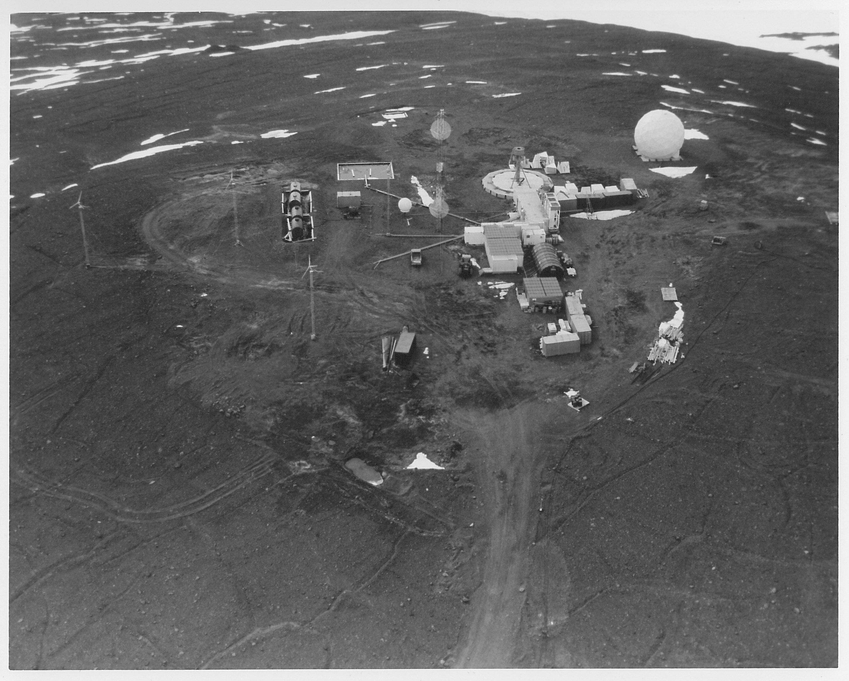 Aerial view of buildings and a white sphere on dark rocky ground.