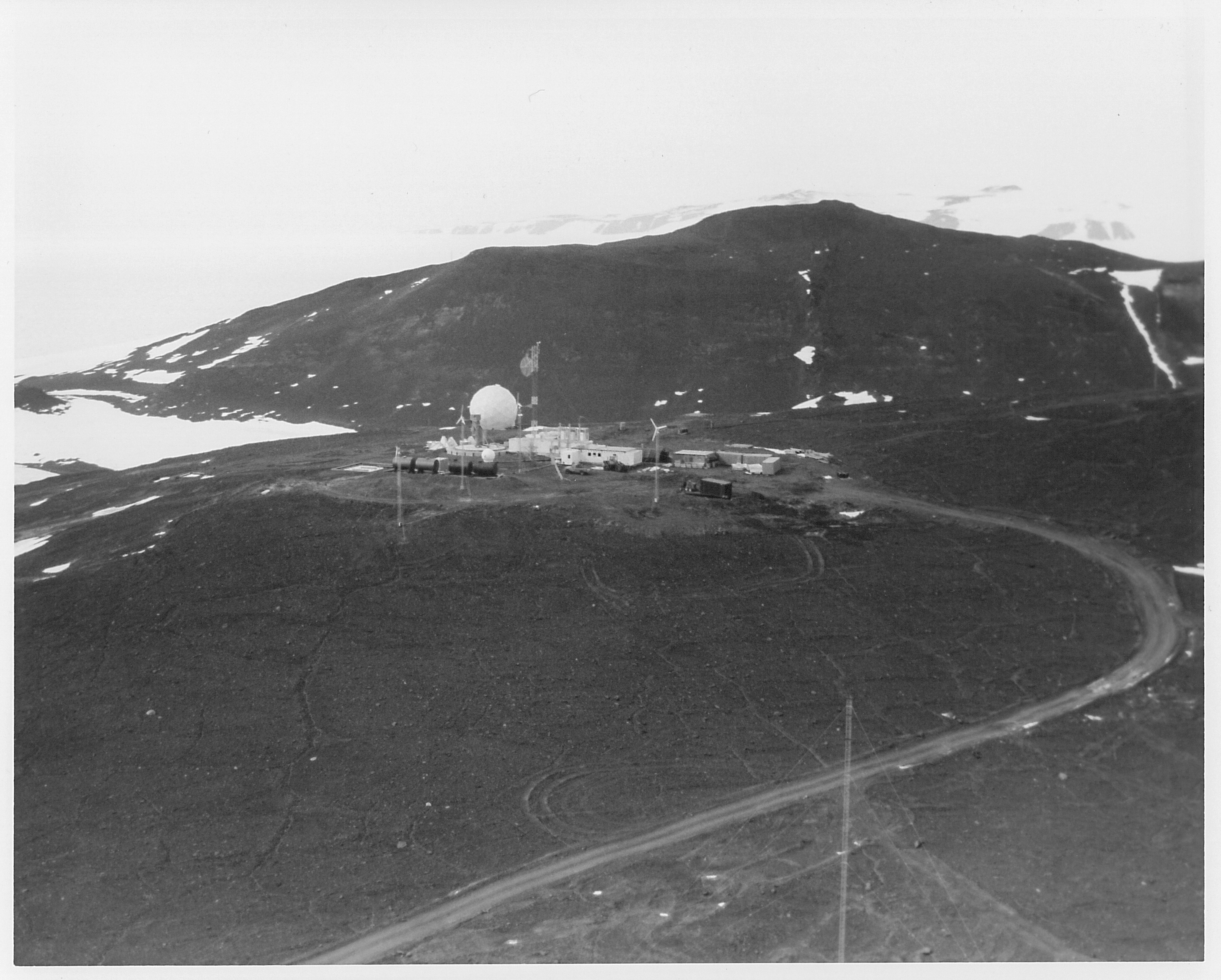 Aerial view of buildings and a white sphere on dark rocky ground.