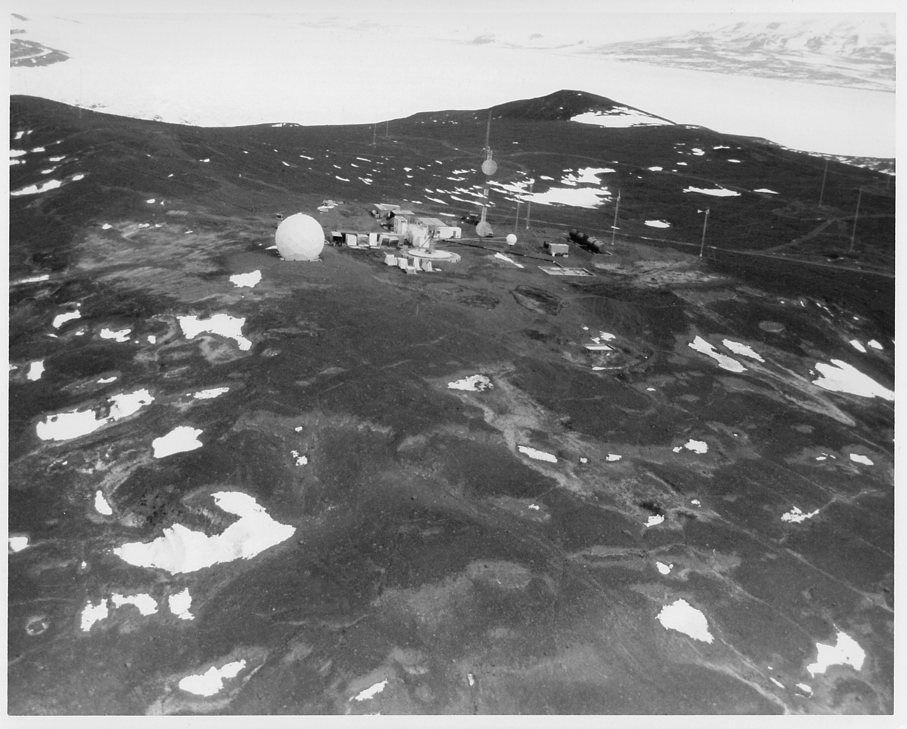 Aerial view of buildings and a white sphere on dark rocky ground.