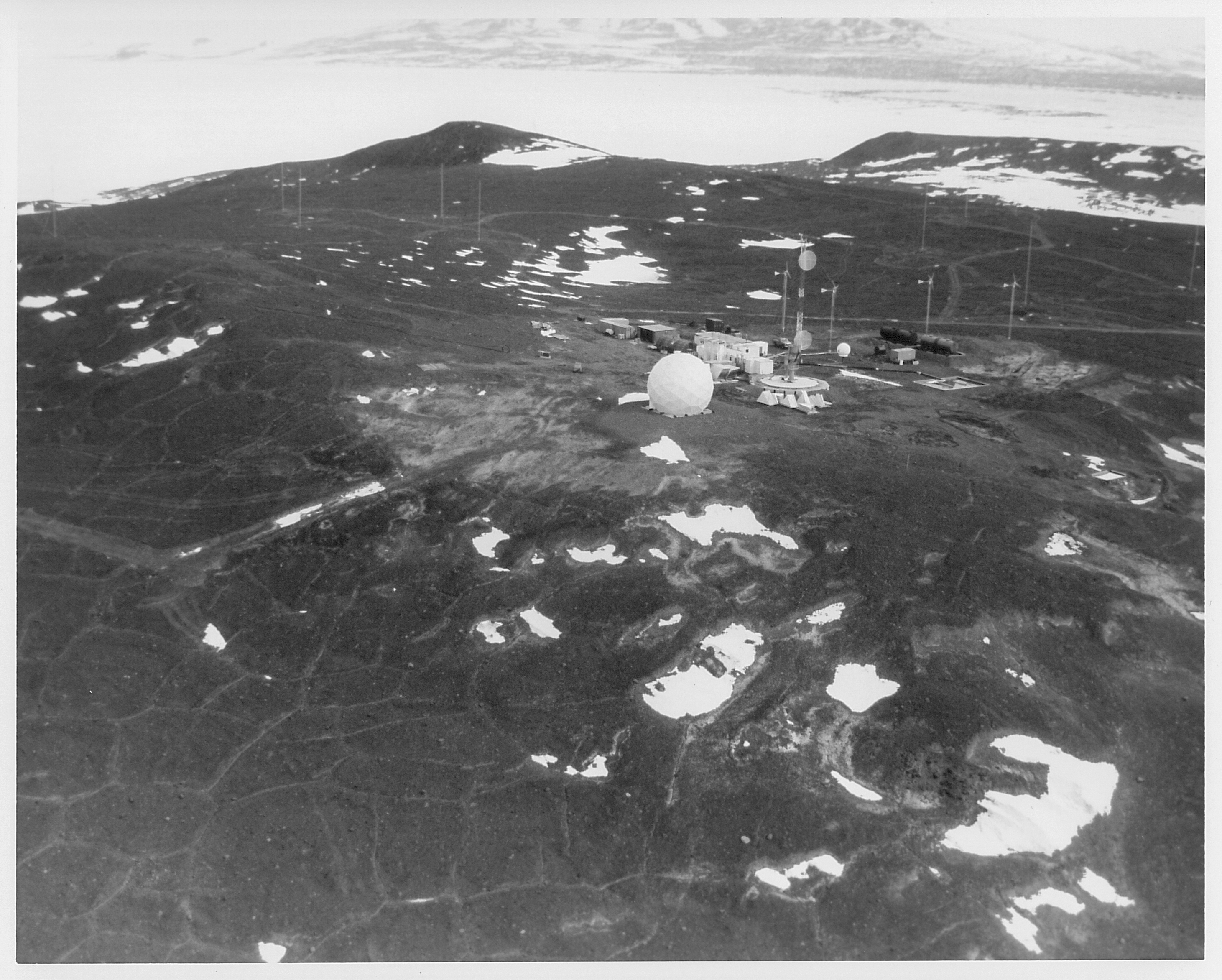 Aerial view of buildings and a white sphere on dark rocky ground.