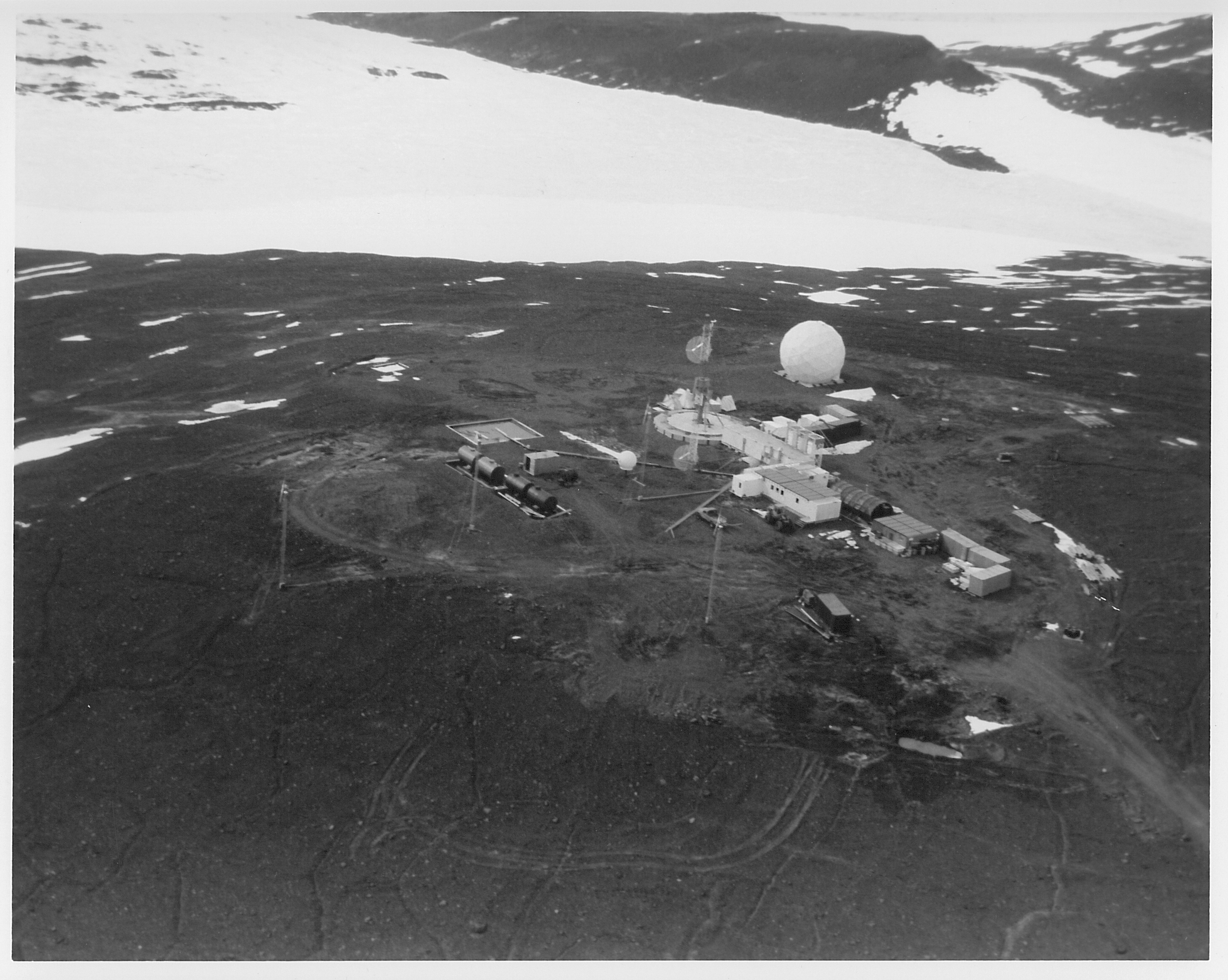 Aerial view of buildings and a white sphere on dark rocky ground.