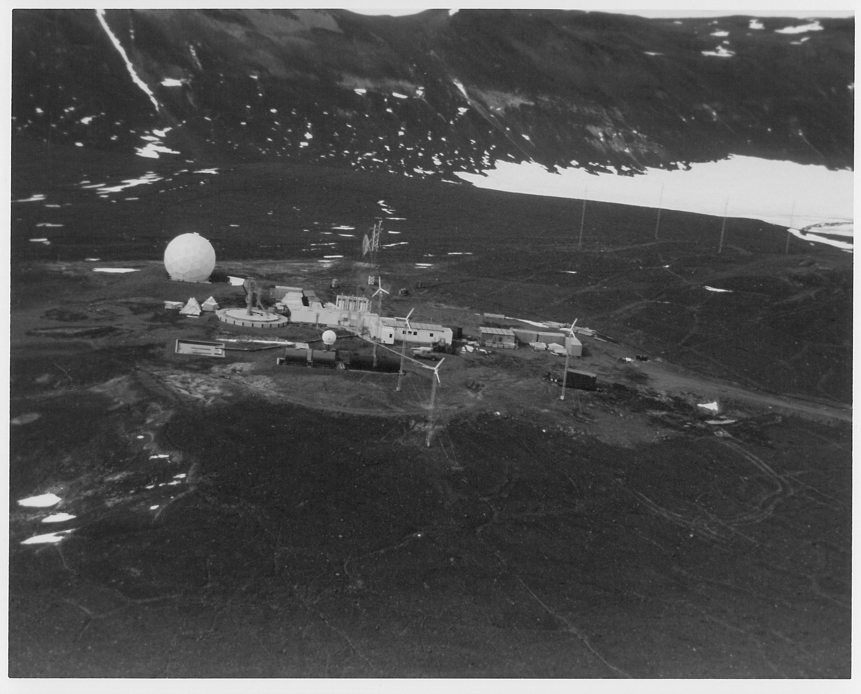 Aerial view of buildings and a white sphere on dark rocky ground.