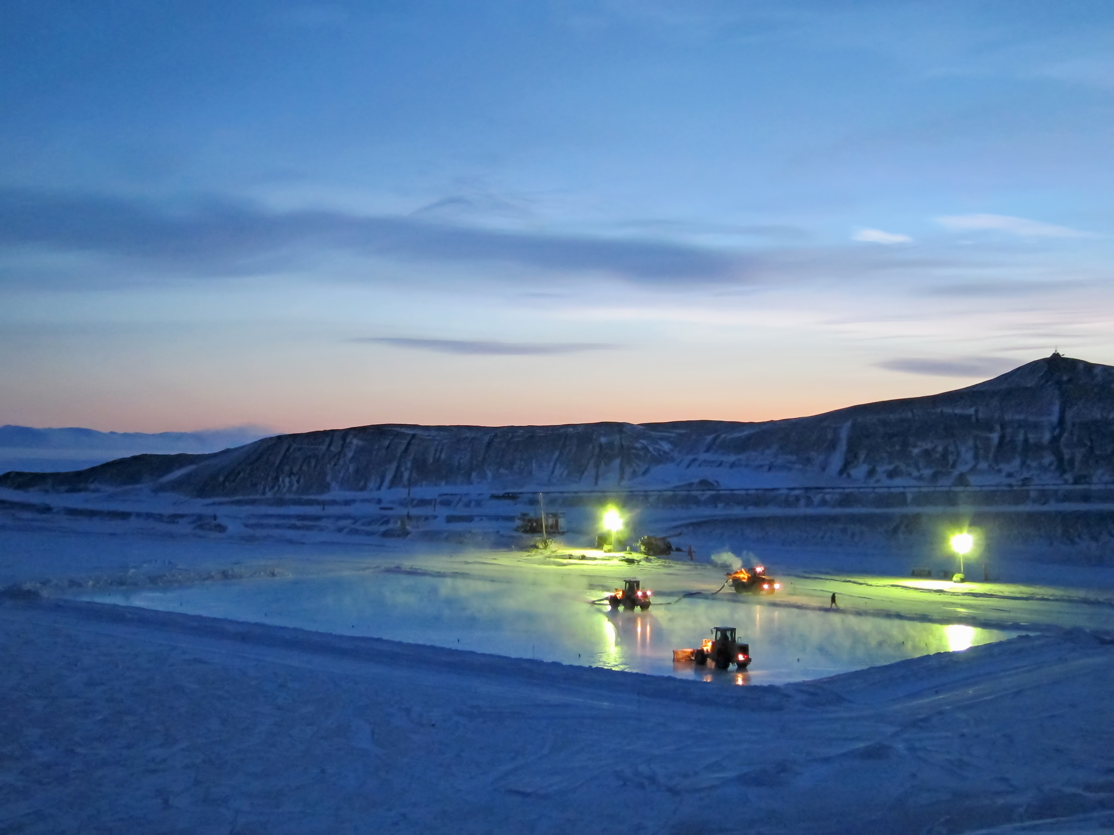 Several large tractors work on an icy surface at night.