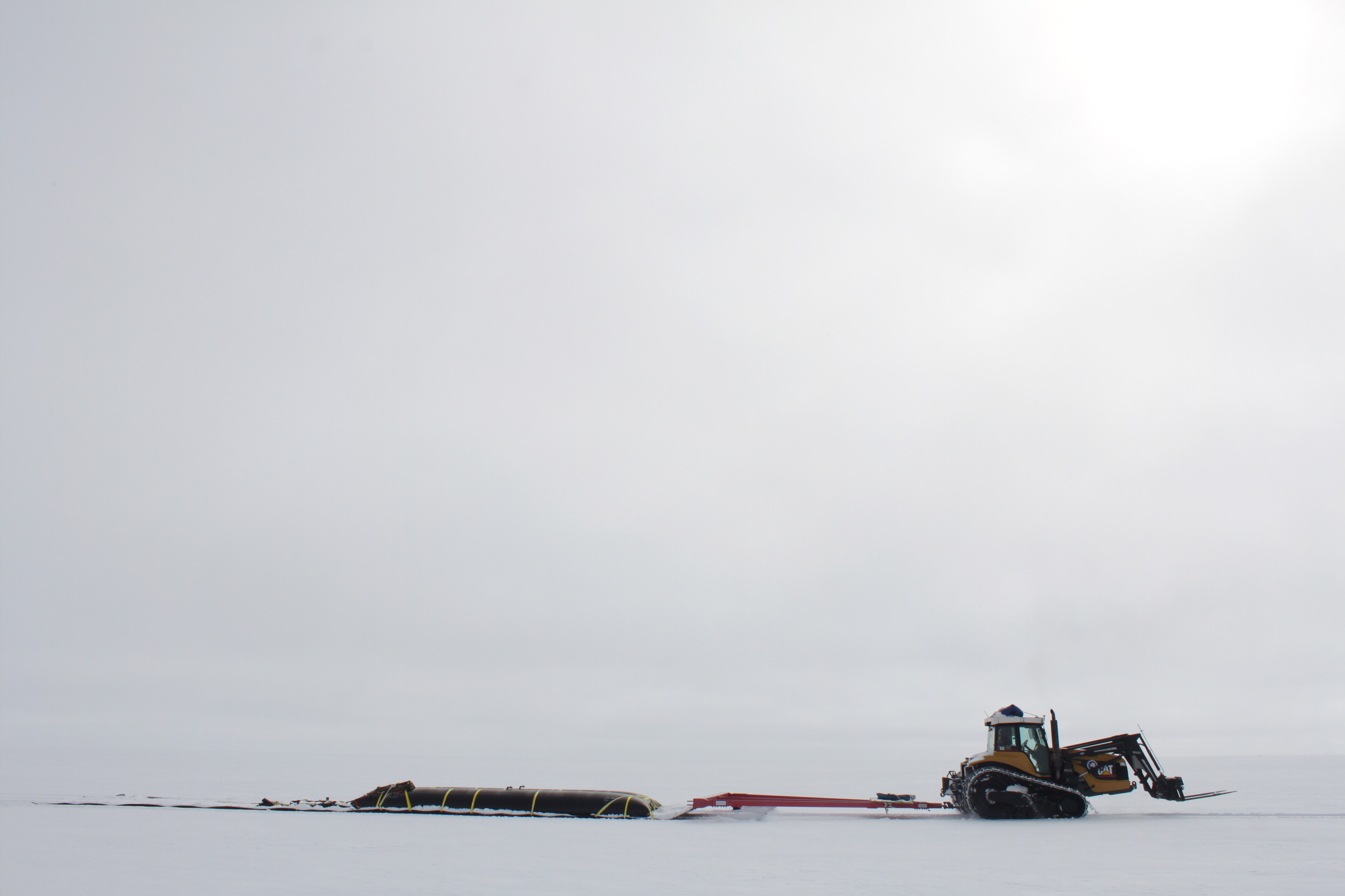 A tractor pulling fuel bladders across the snow.