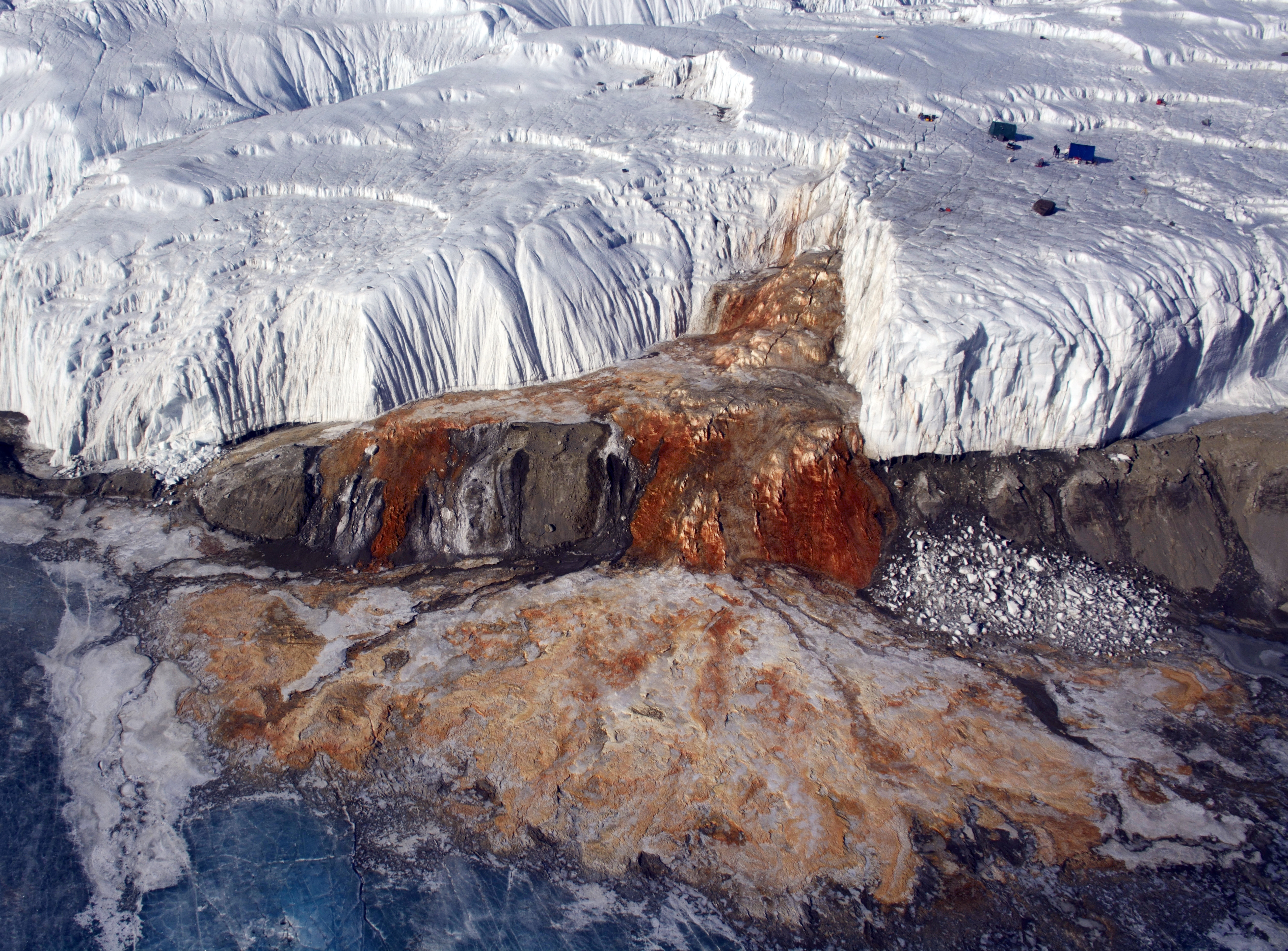 Aerial view of a glacier with a red waterfall.