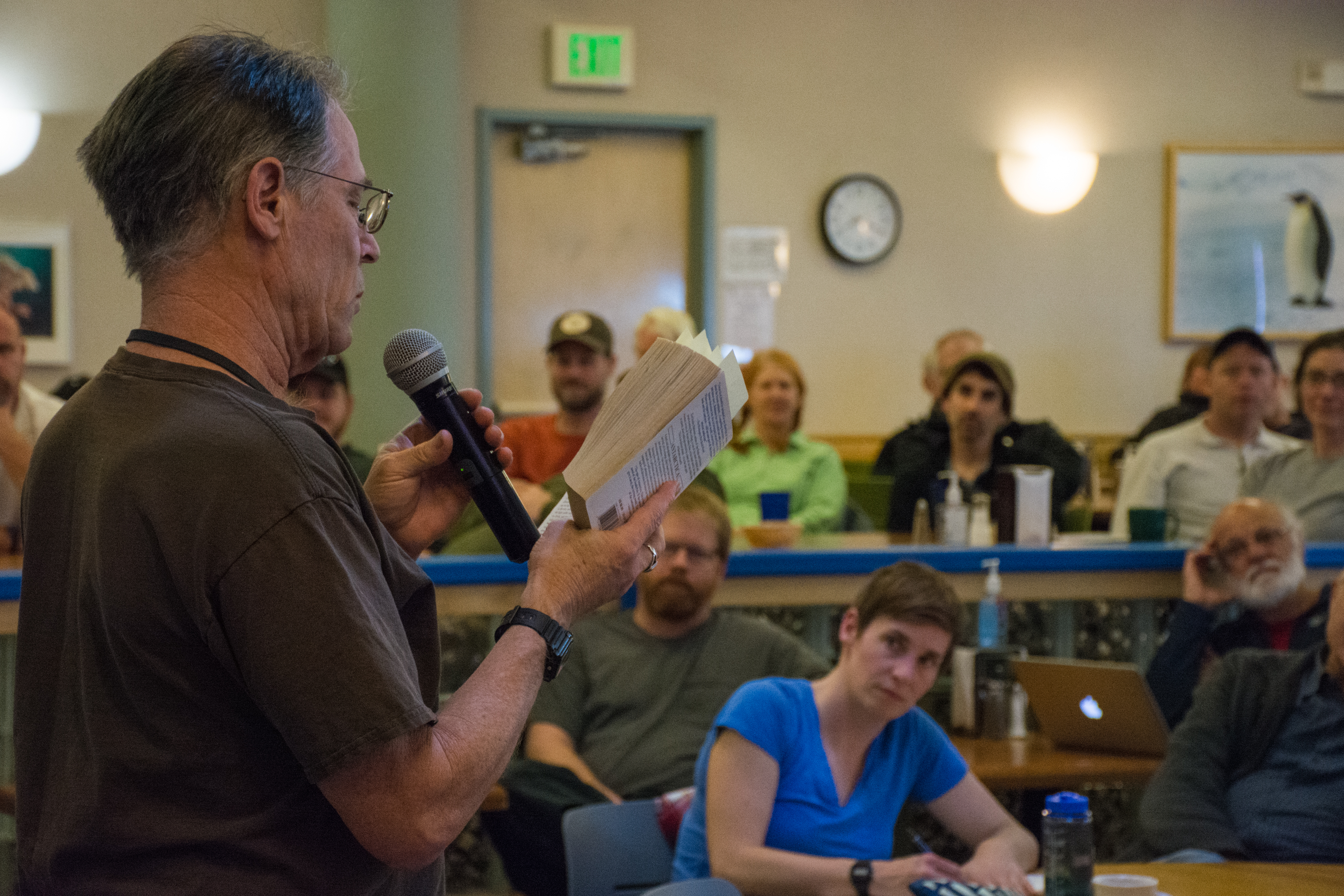 A man reading from a book in front of a group.