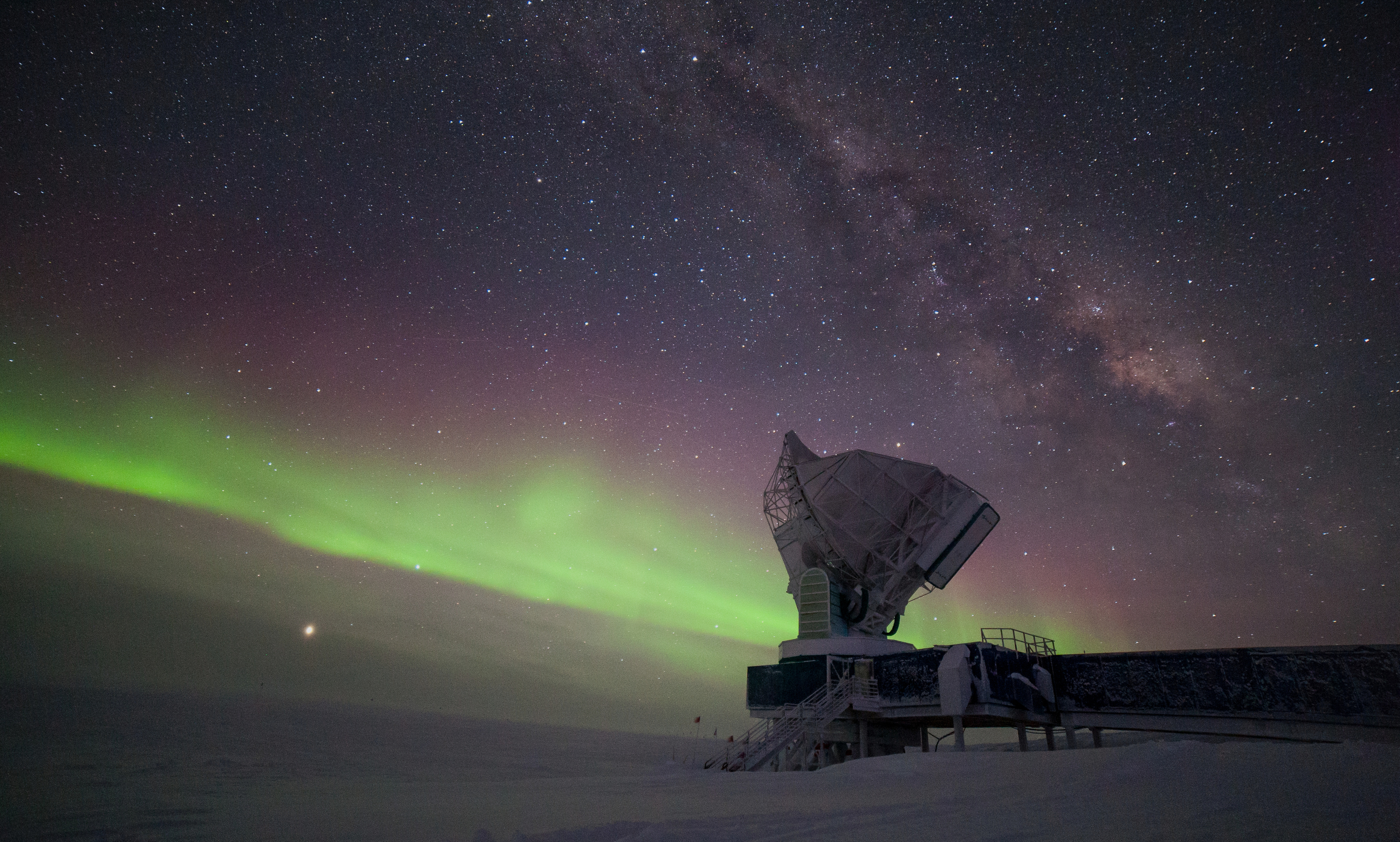 Auroras and the Milky Way fill a night sky over a telescope.
