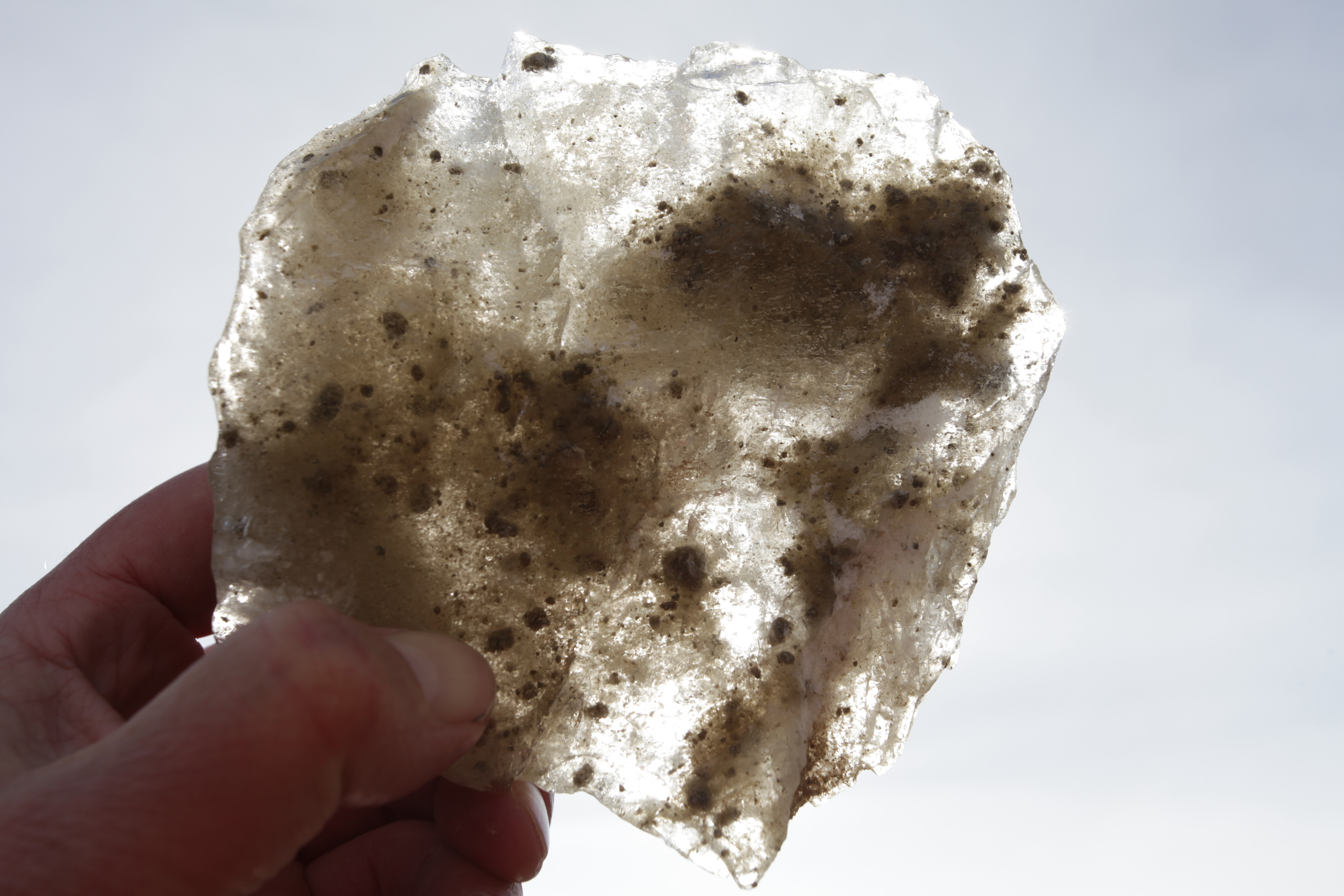 A piece of ice with dirt in it being held upwards against the sunlight.