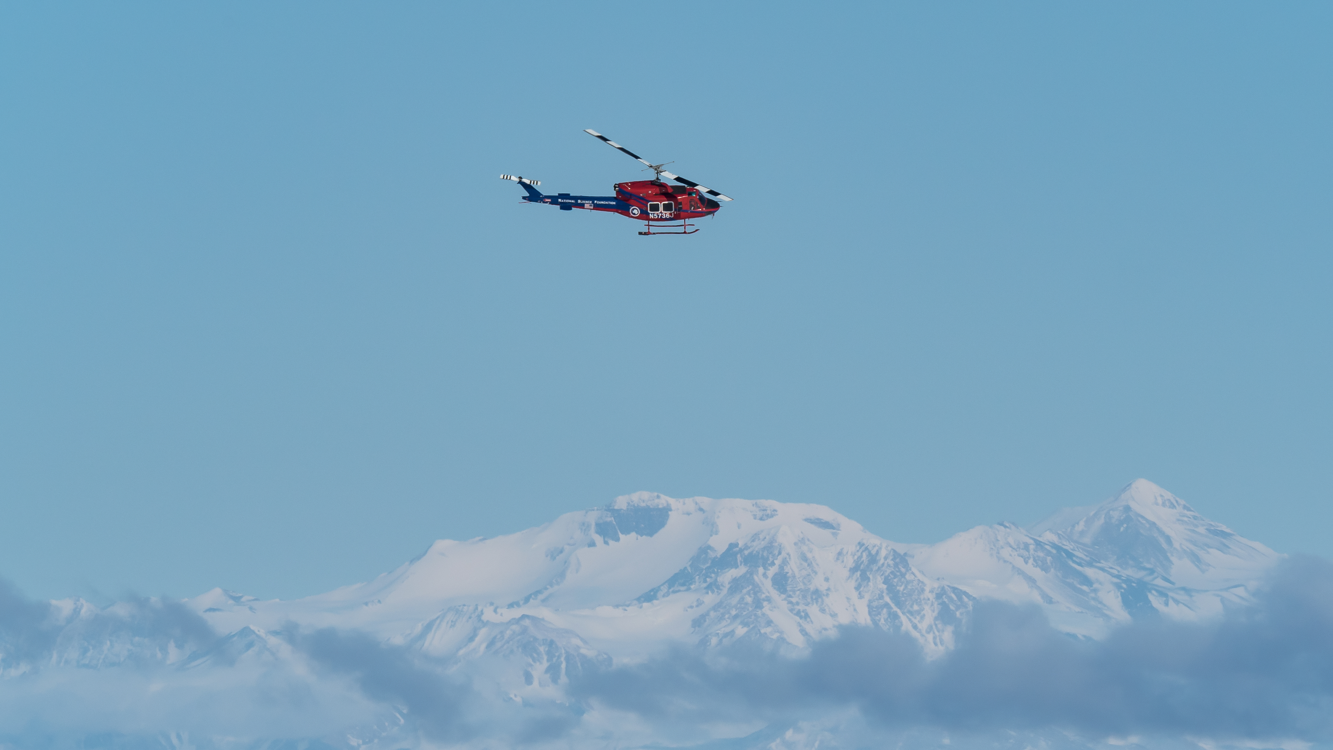 A helicopter flying over snowy mountains.