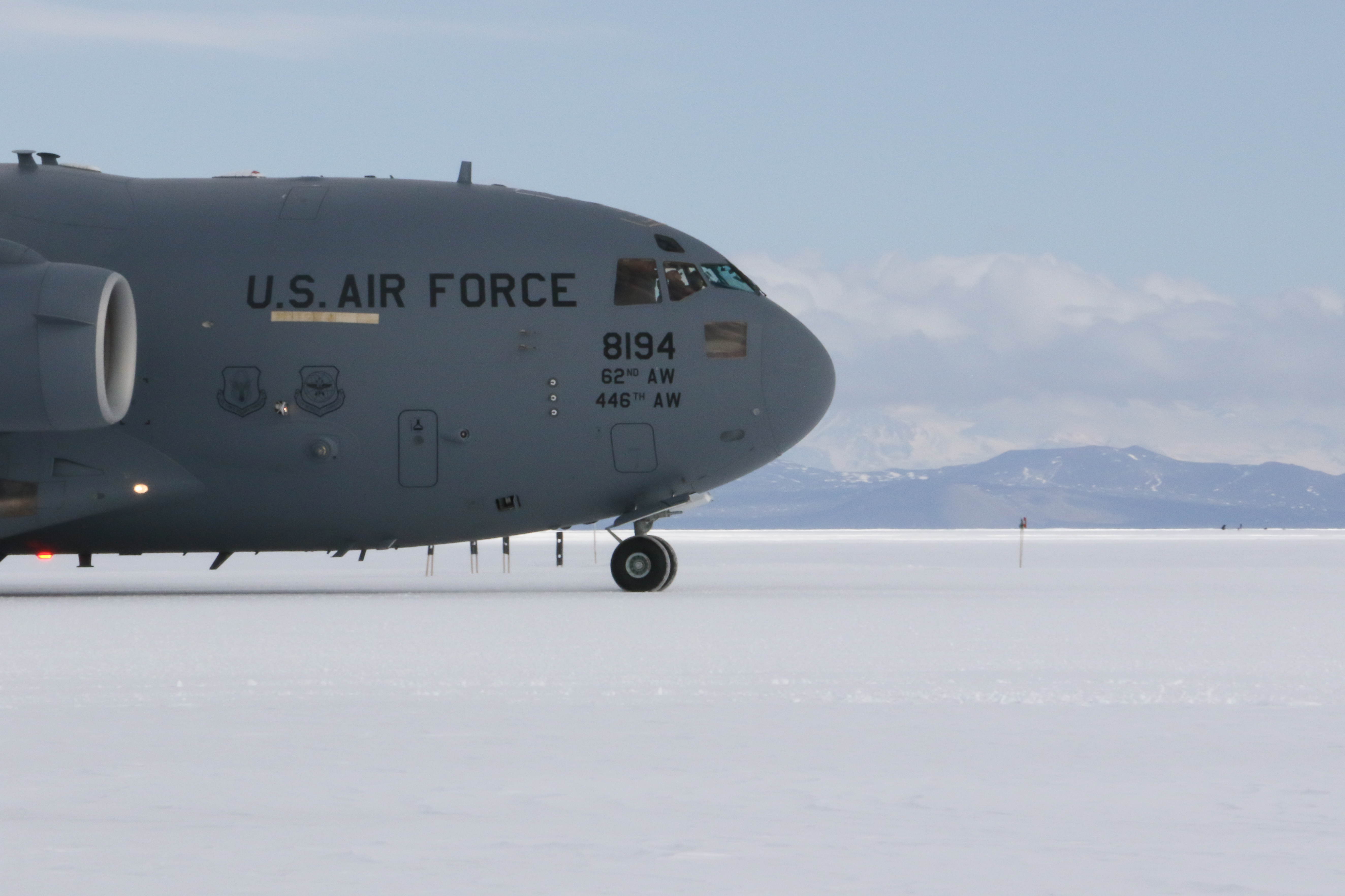 An airplane nose and snowy mountains in the background.