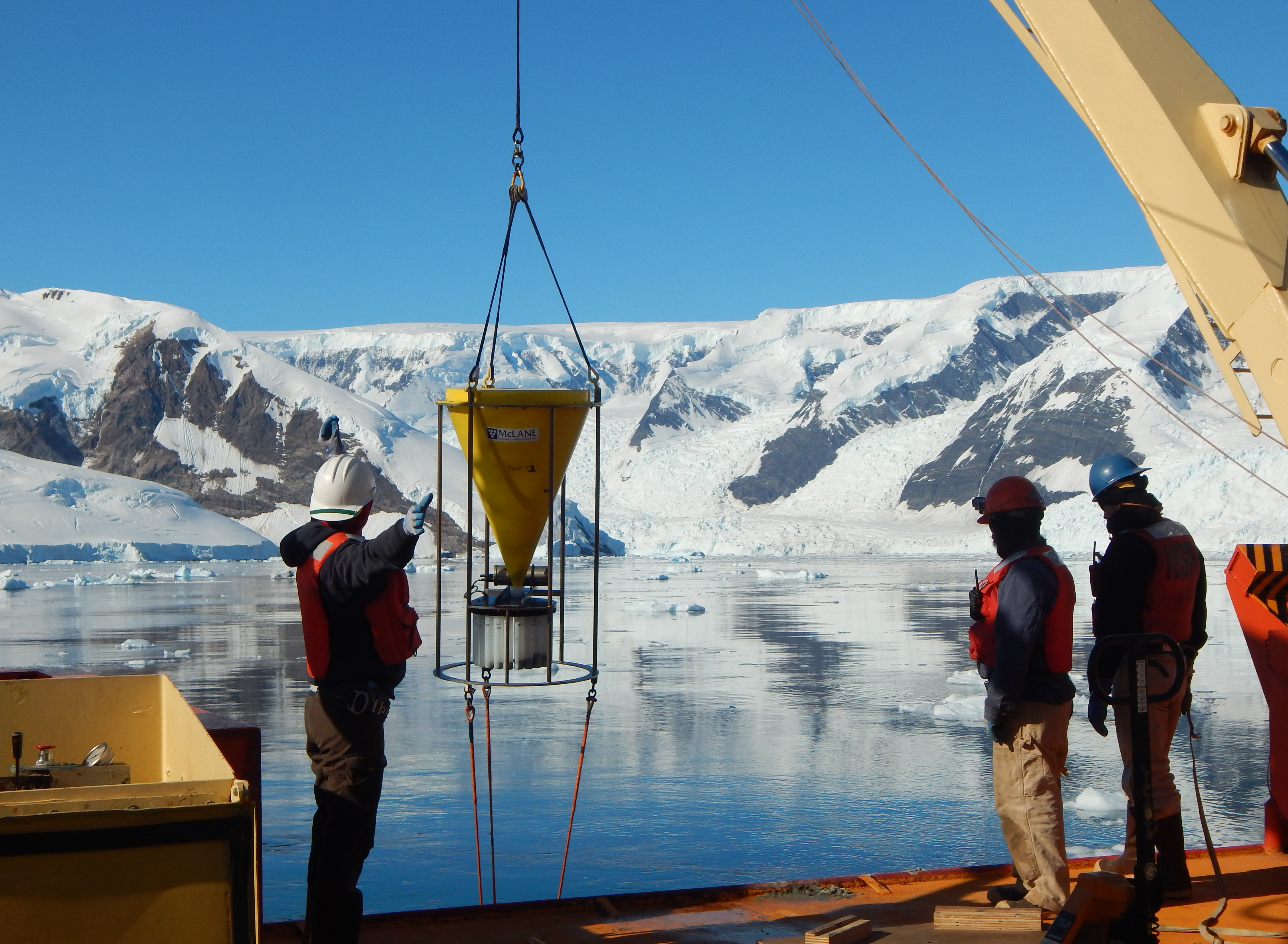 Three people lowering an instrument over the side of a ship.