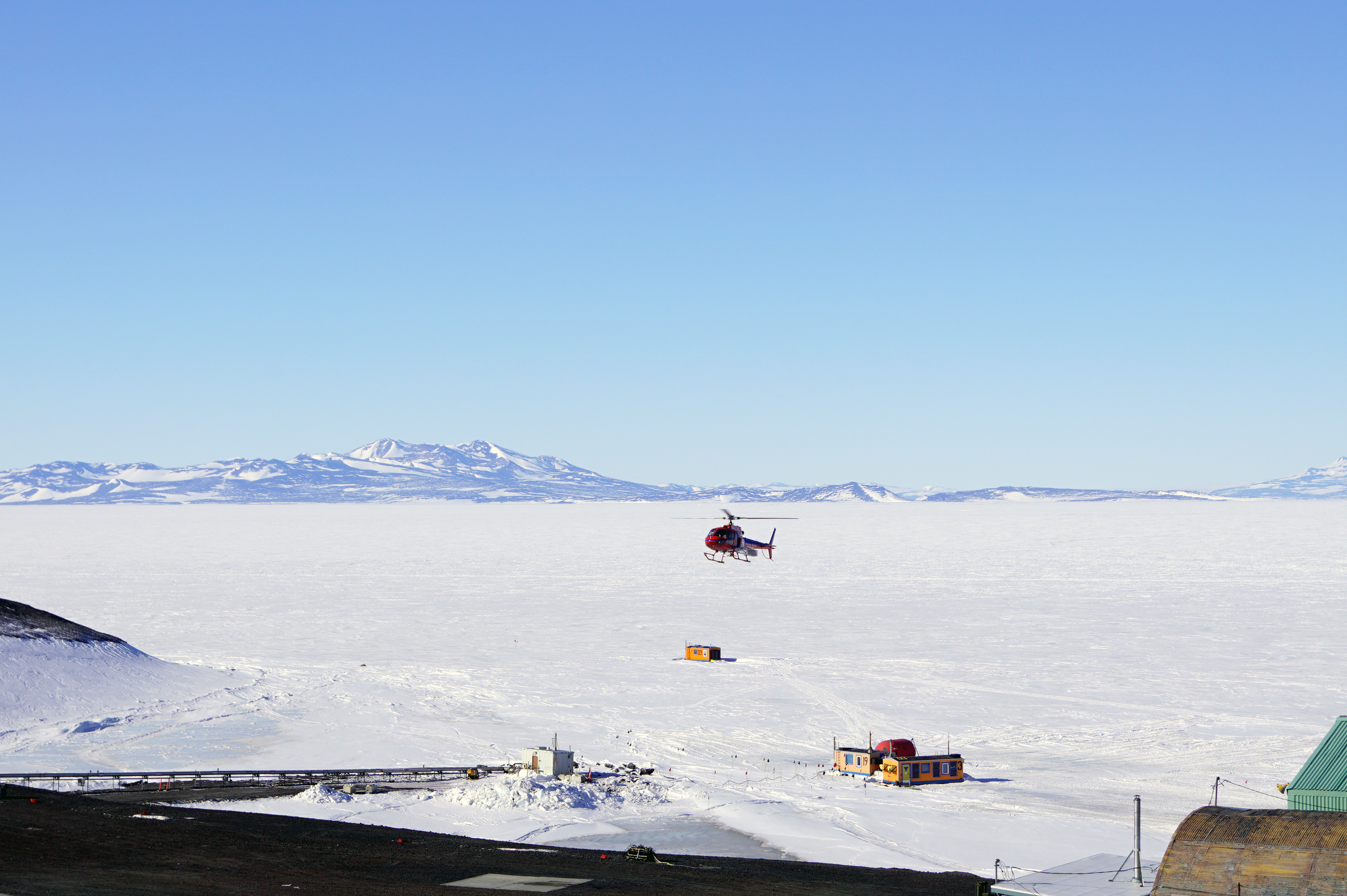 A helicopter flies over snow-covered landscape.