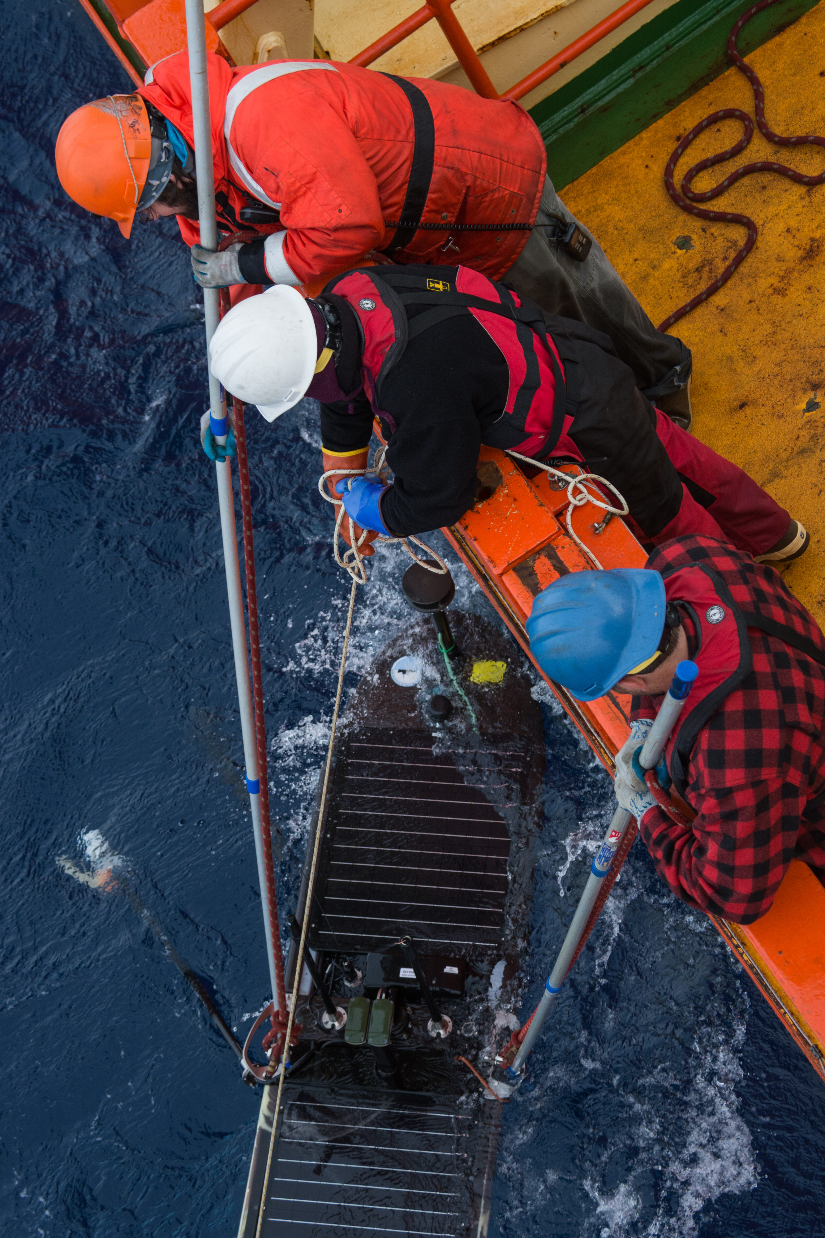 Three people on the edge of a ship retrieving something out of the water.