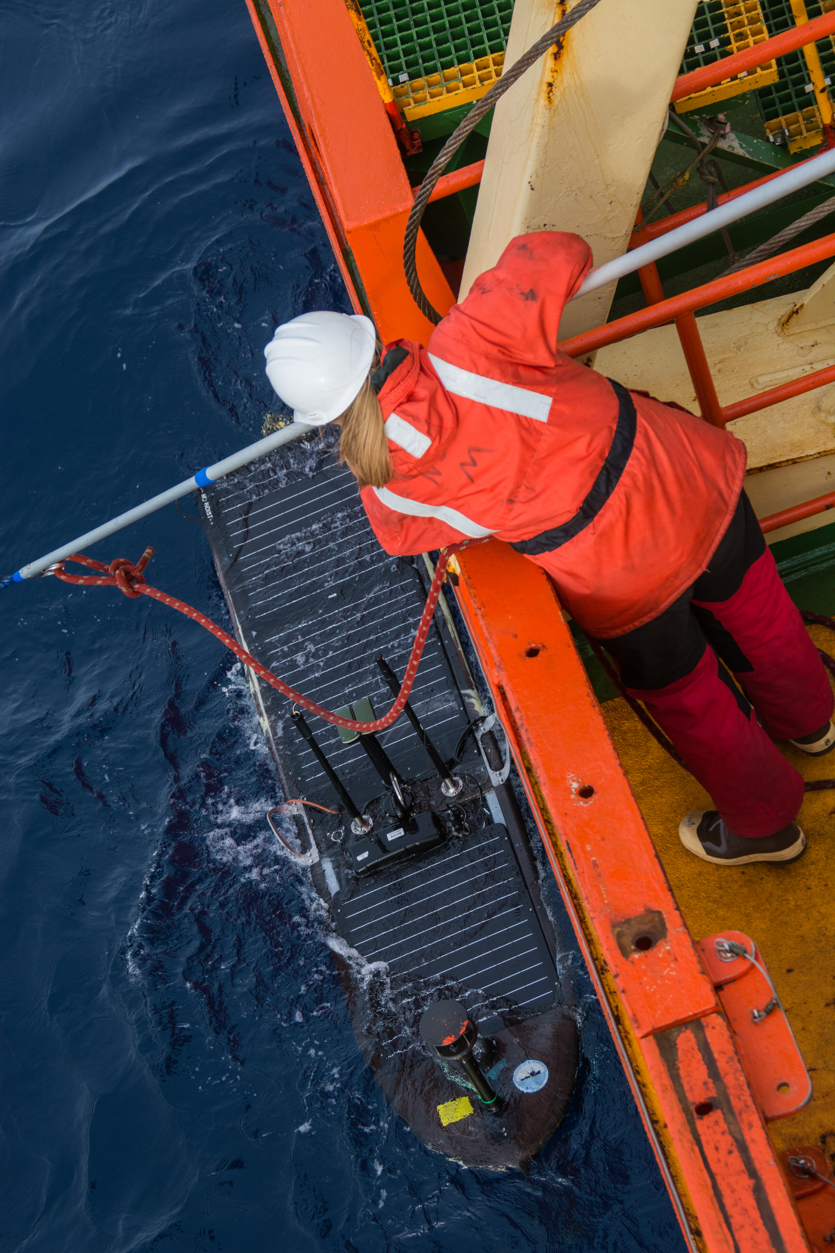 A person on a ship reaching down to get something out of the water.
