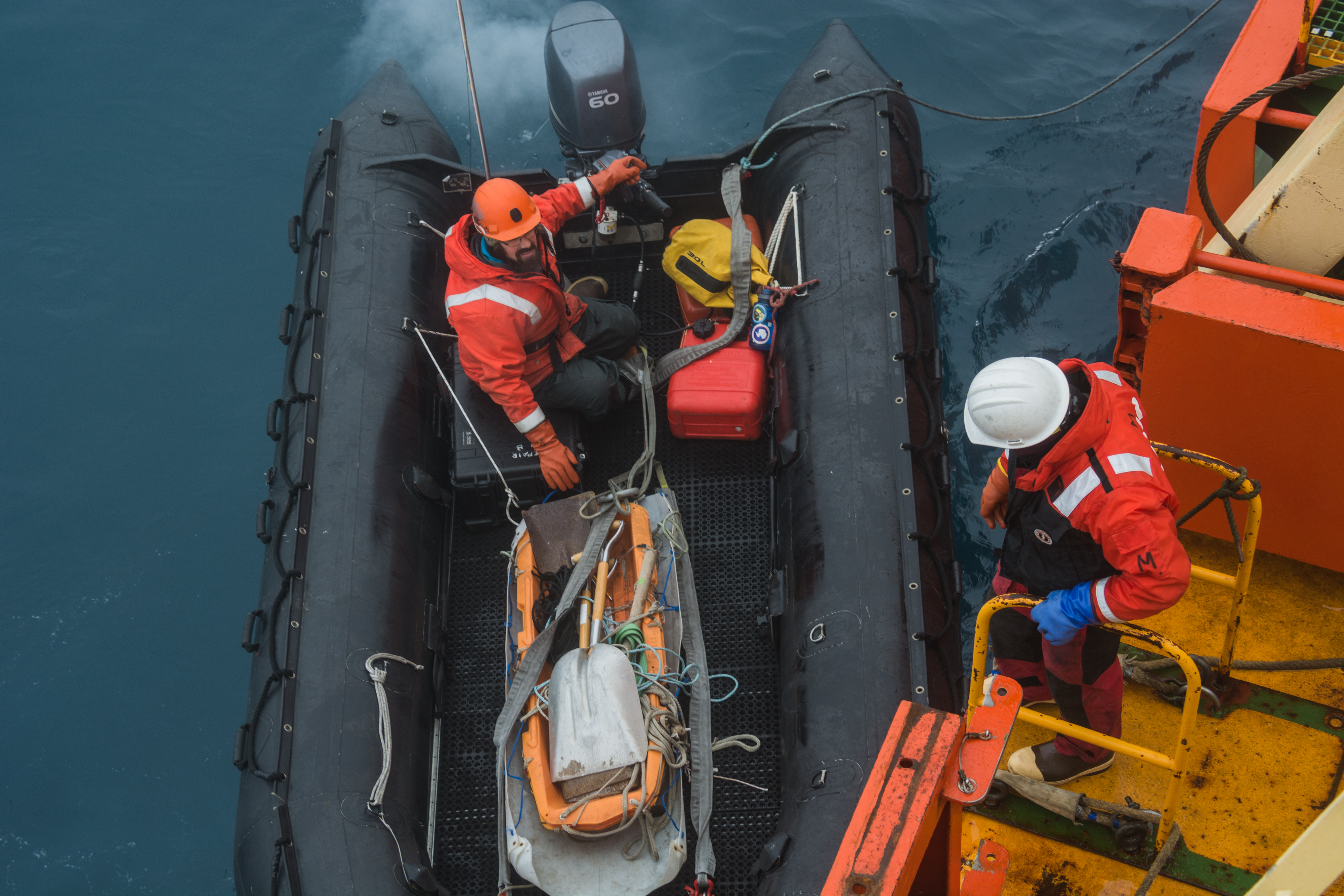 A person onboard a ship assisting another in a smaller boat on the water.