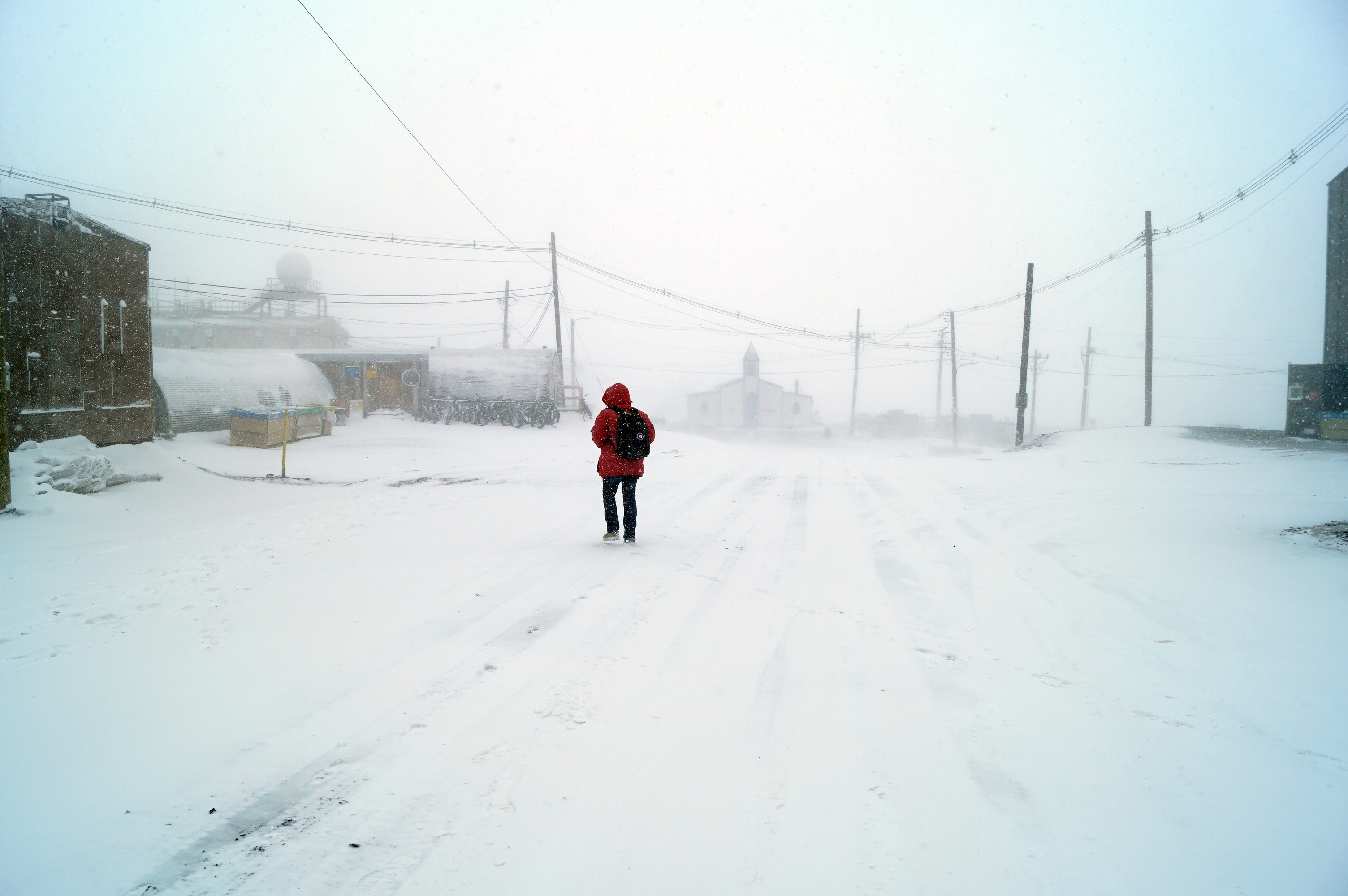 A person in a red jacket walking outside during a snow storm.