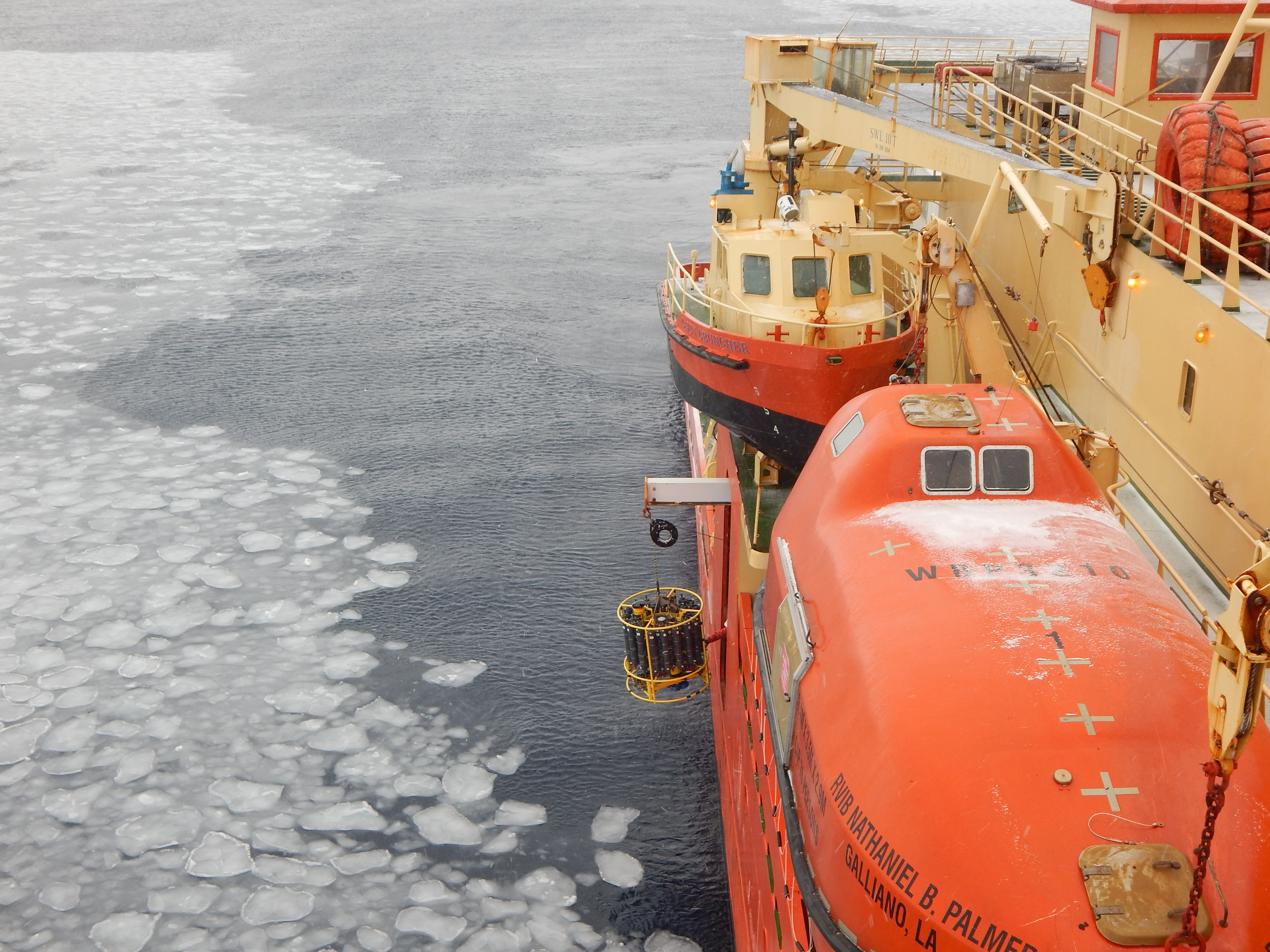 An instrument is lowered over the side of a ship into icy water.