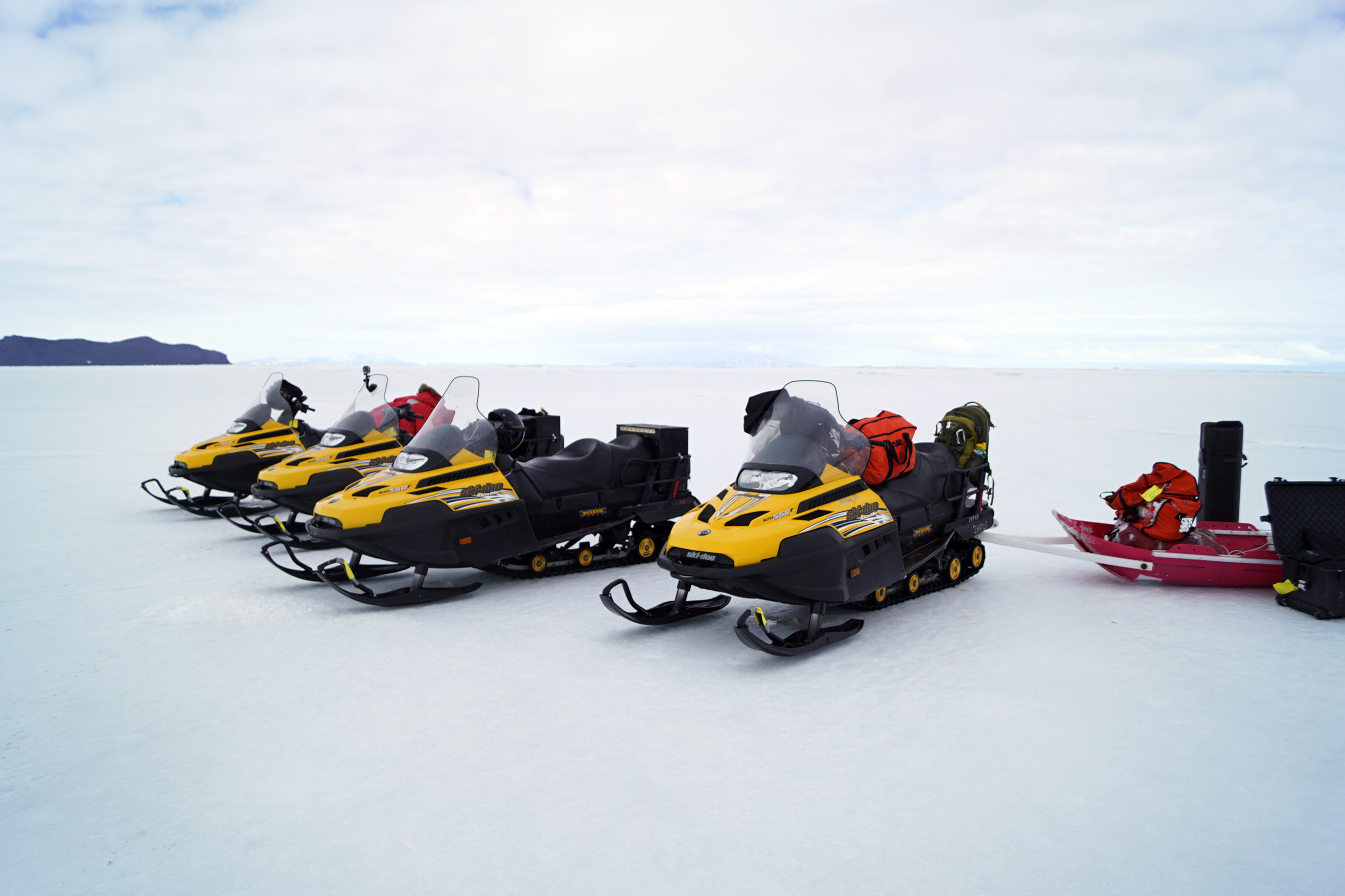 Four yellow snowmobiles parked on ice.