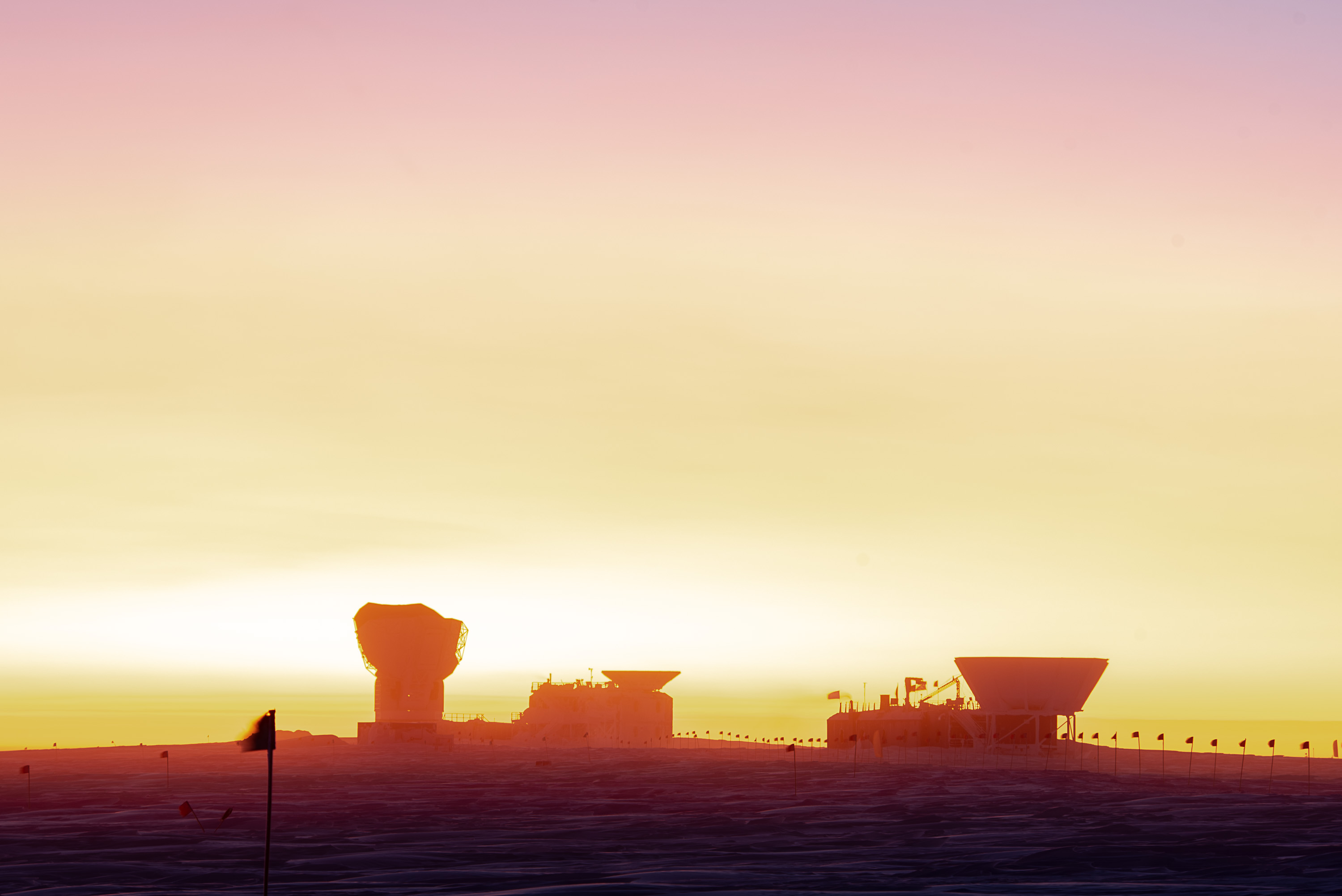 A view of the sunrise behind buildings on a snow-covered landscape.