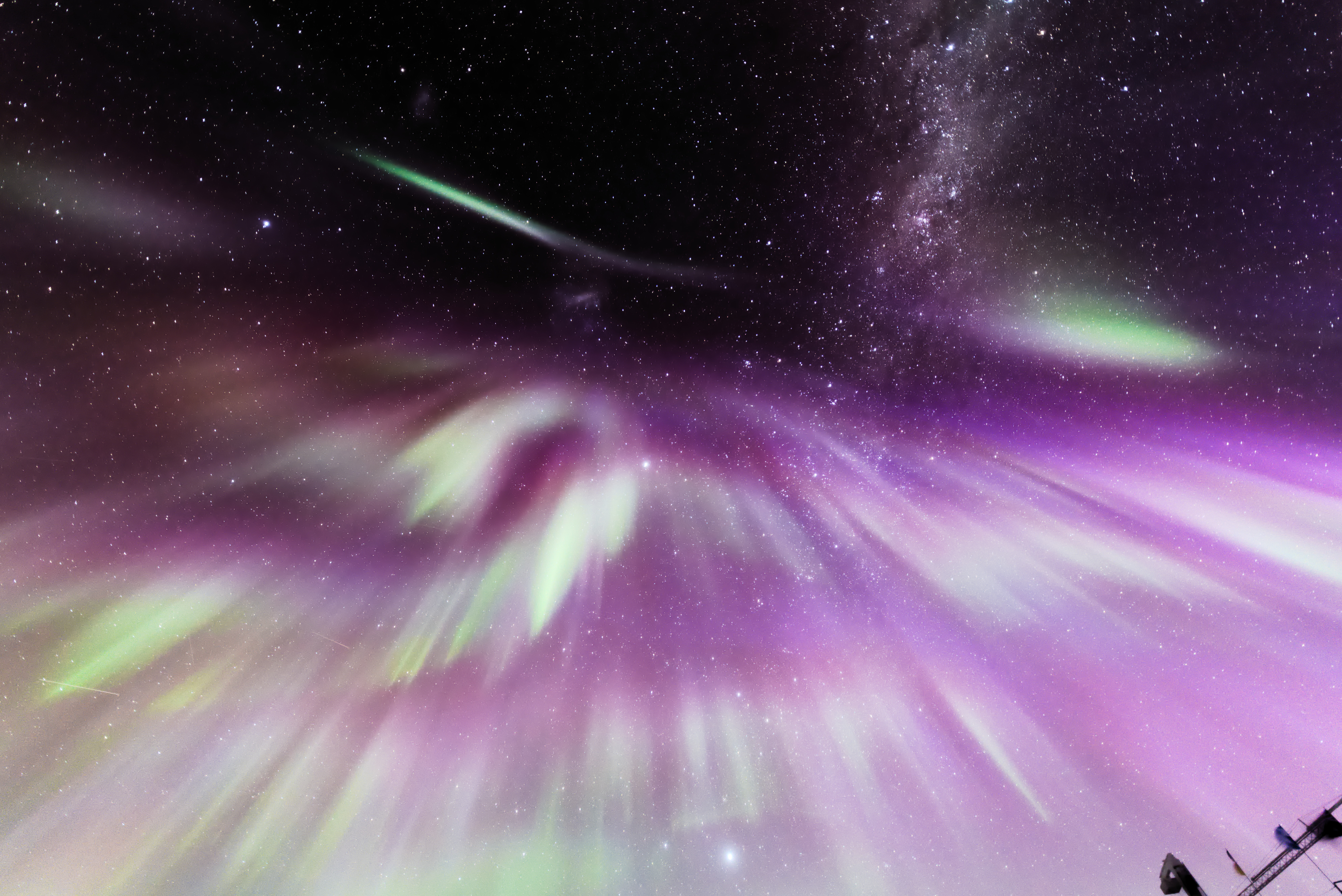Green and purple auroras as streaks in the night sky, looking up from the ground. 