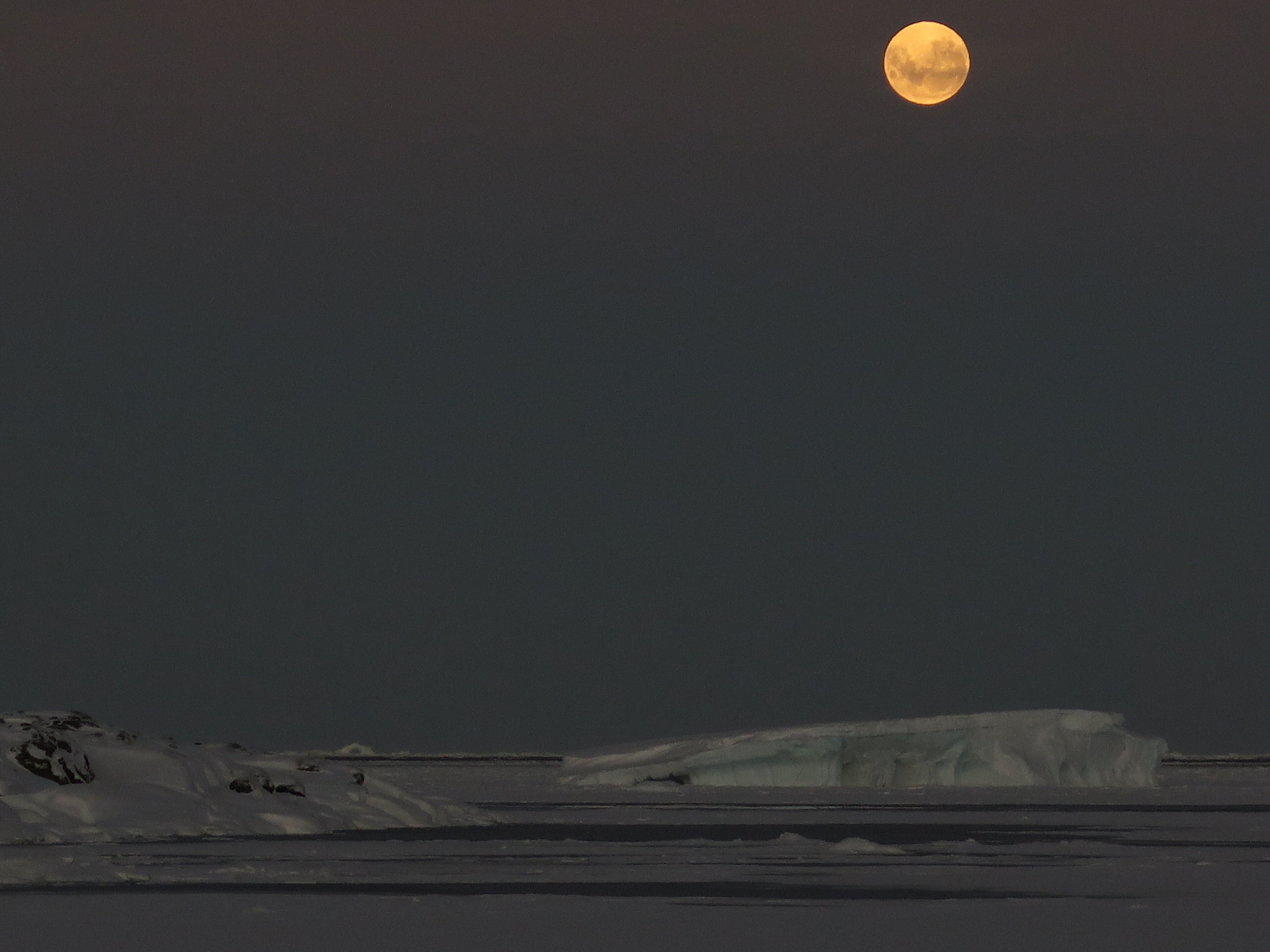 A full moon over snow and water.