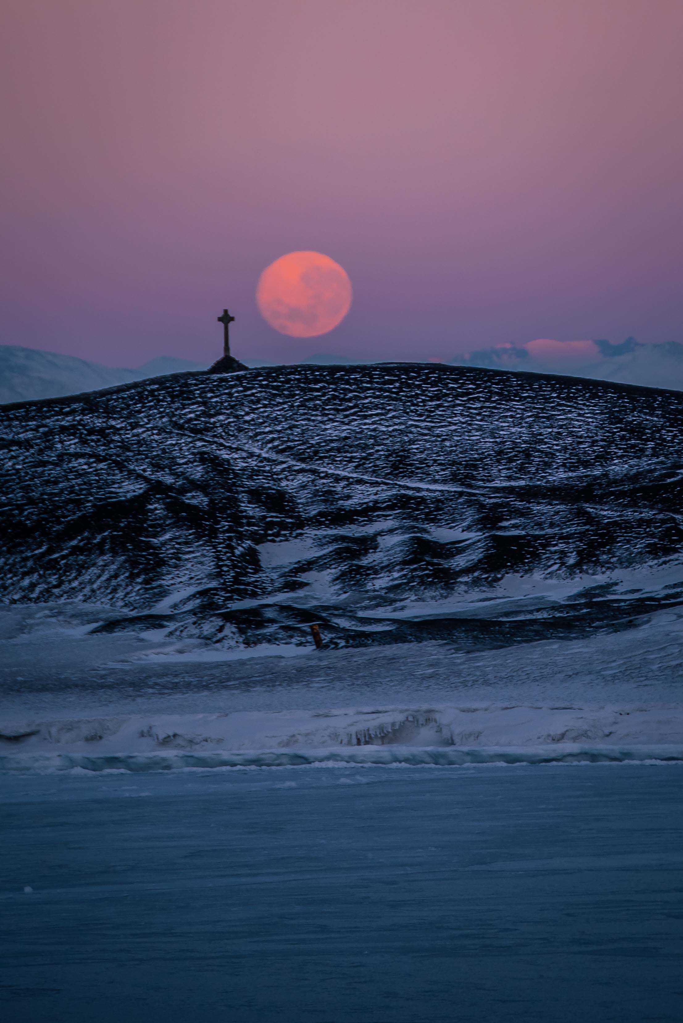 A full moon over a hill that has a cross on top of it.