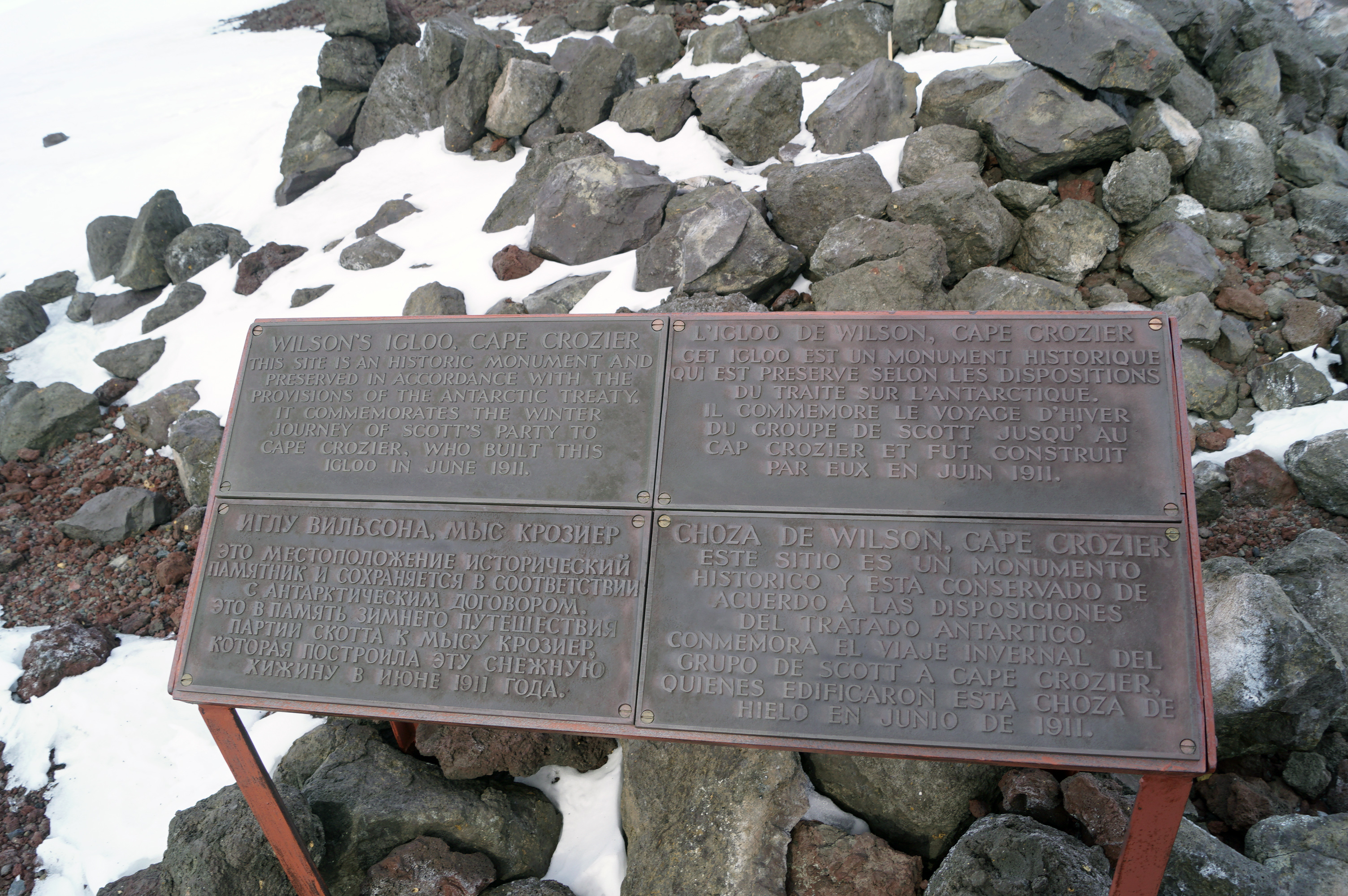 A metal sign next to a rocky landscape.