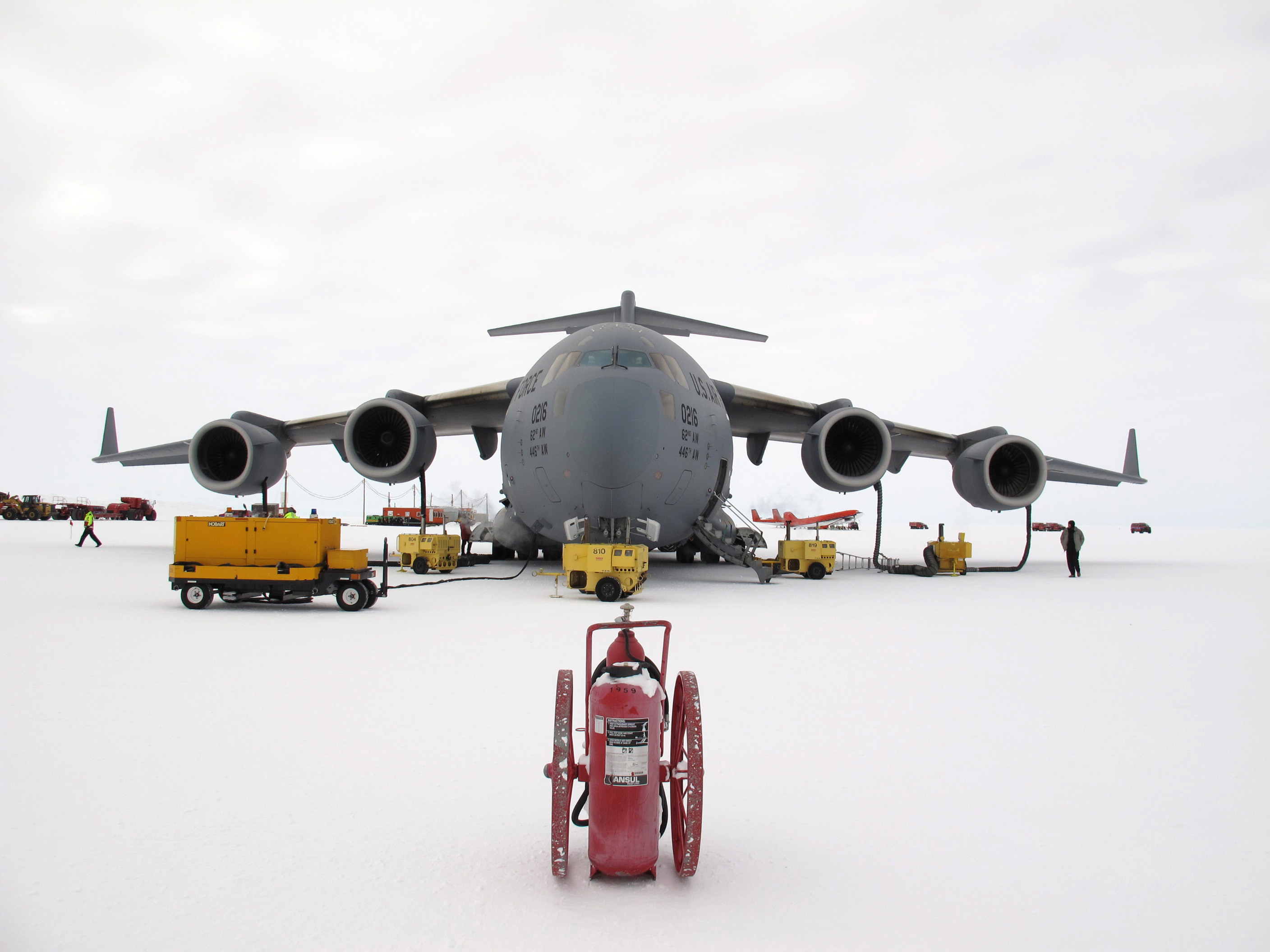 Equipment surrounds a large military jet on an icy surface.