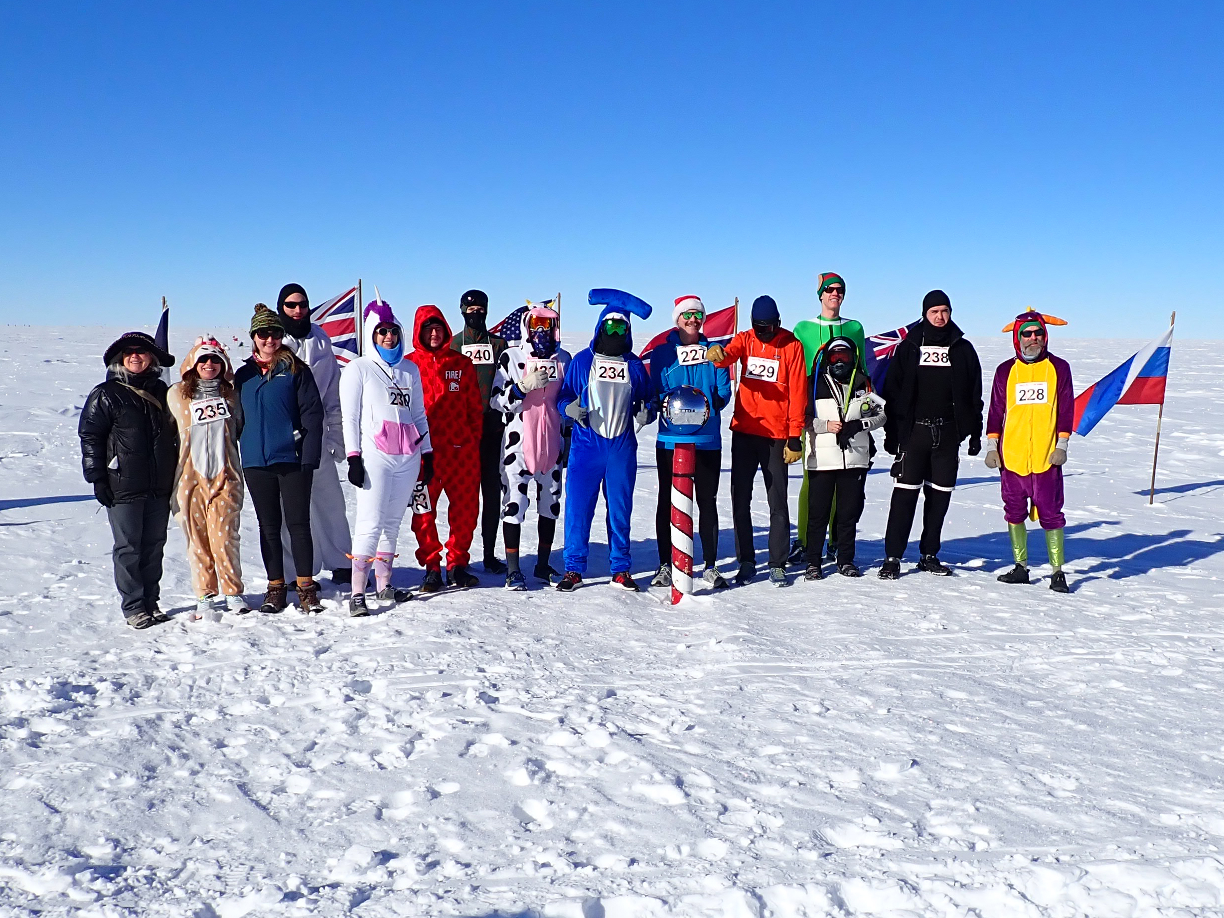 A group of people dressed in costumes with race numbers pinned to them stand outside in the snow.