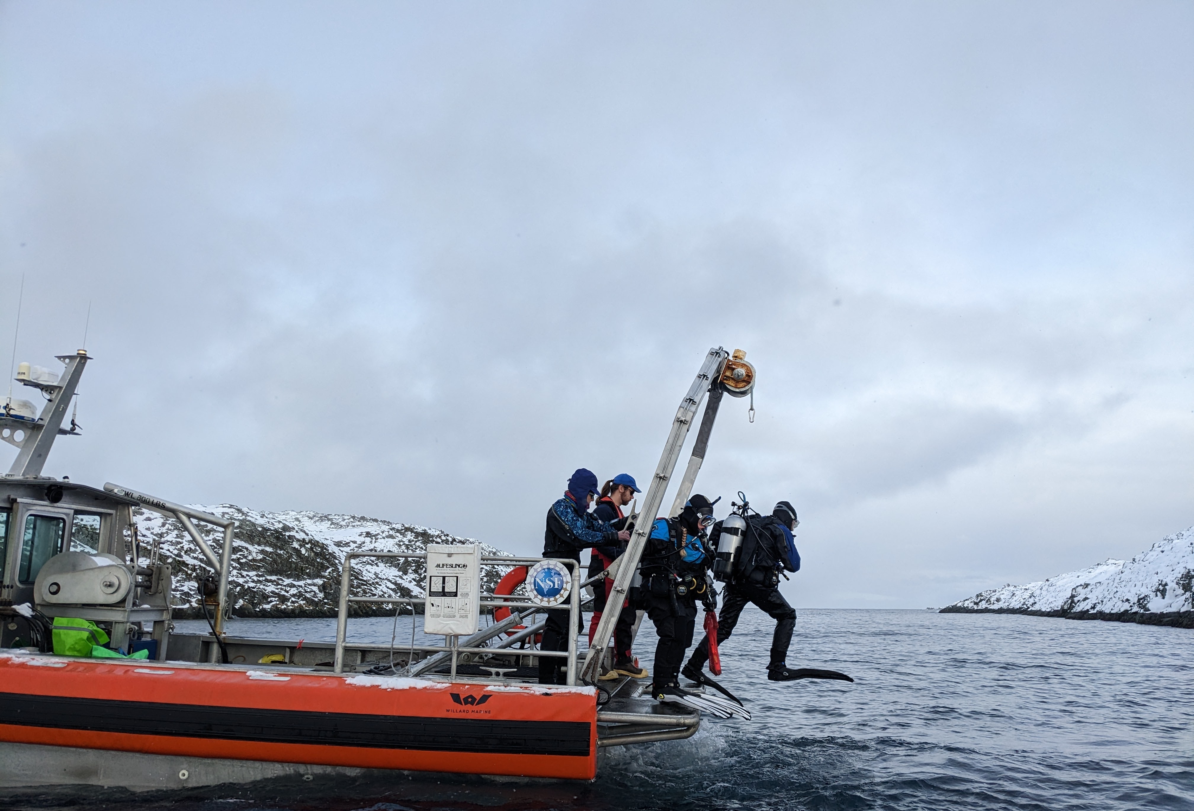 People in diving gear jump off the back of small boat into water