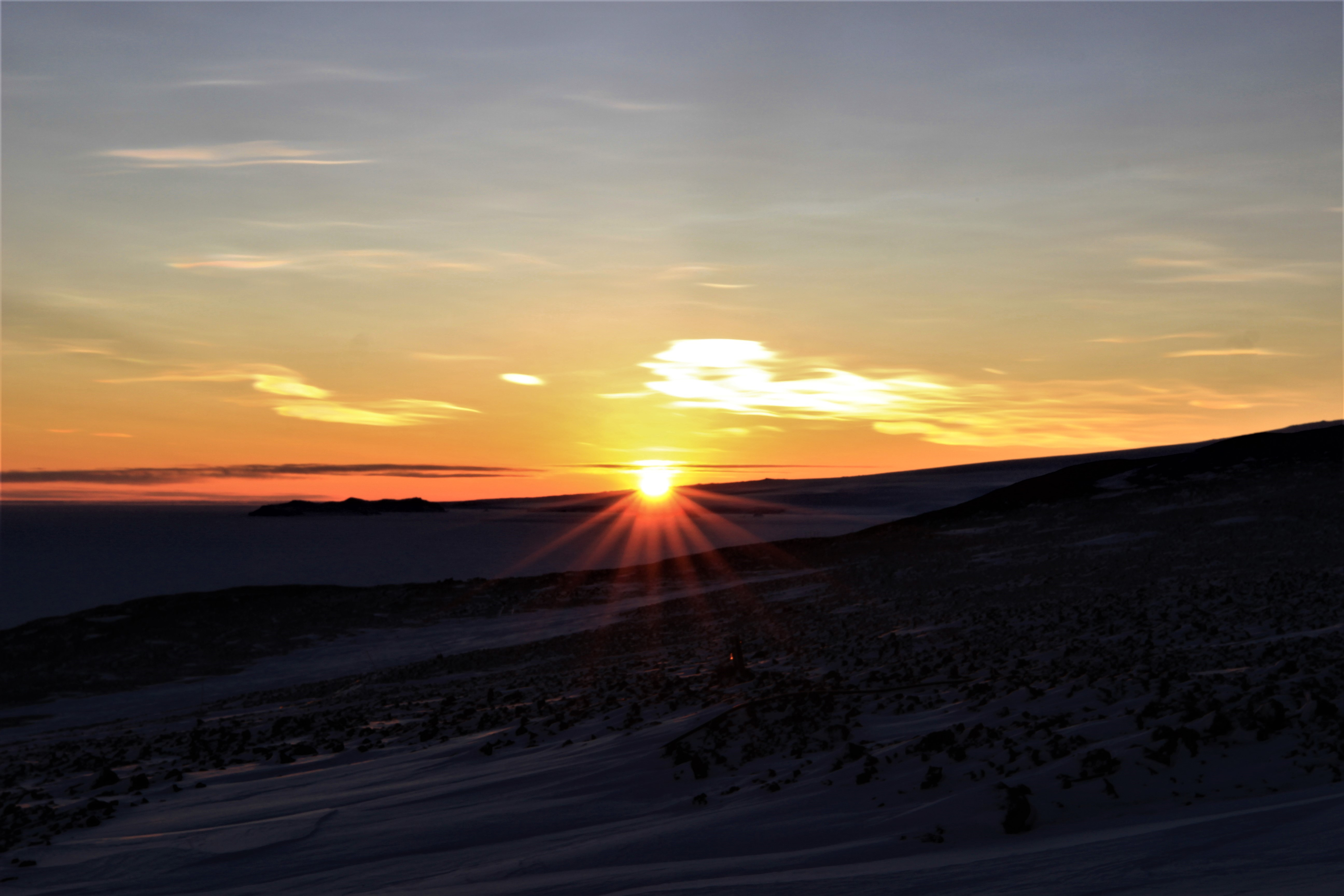 The sun rises behind a hill.