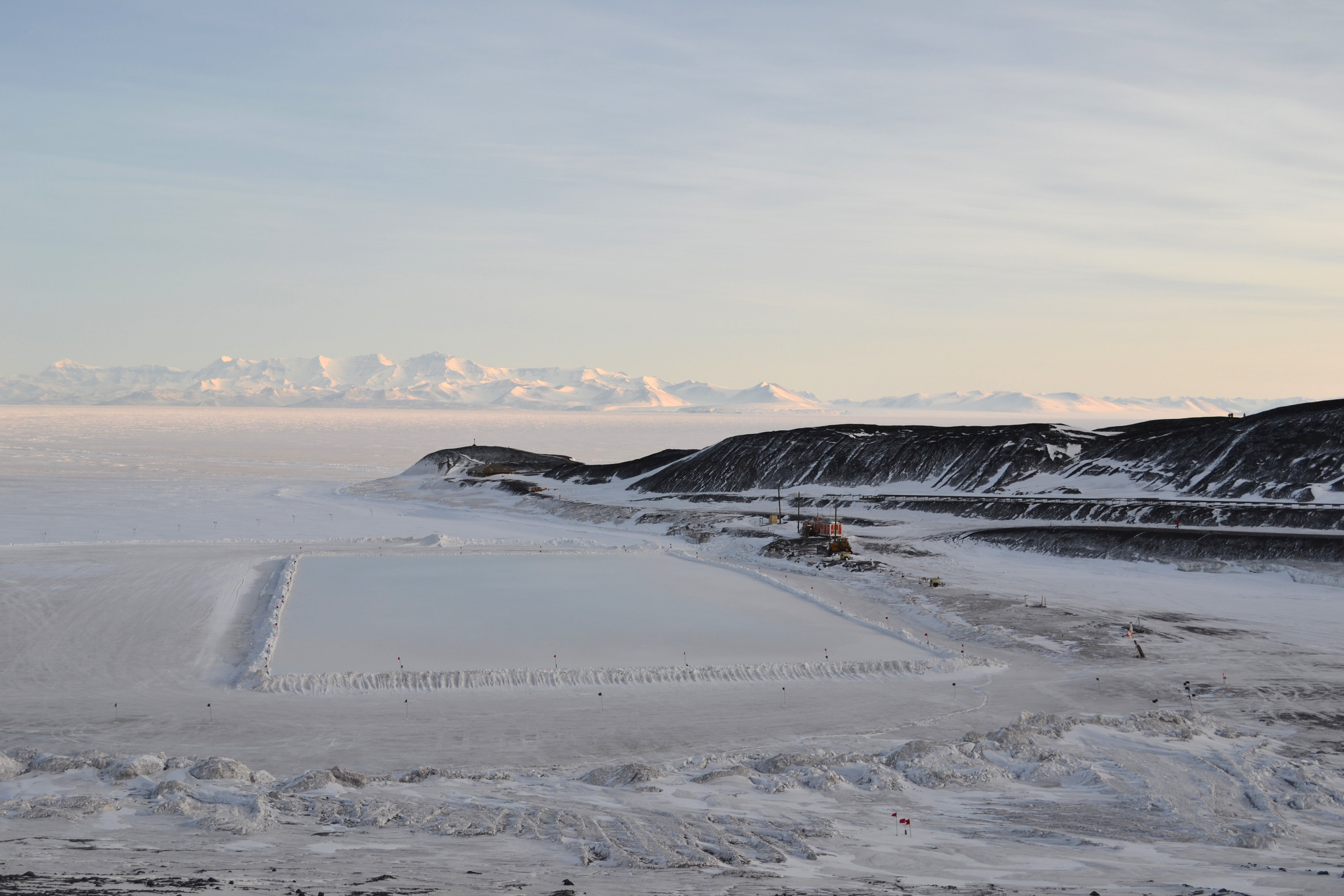 Flat white ice, a shoreline and distant mountains.