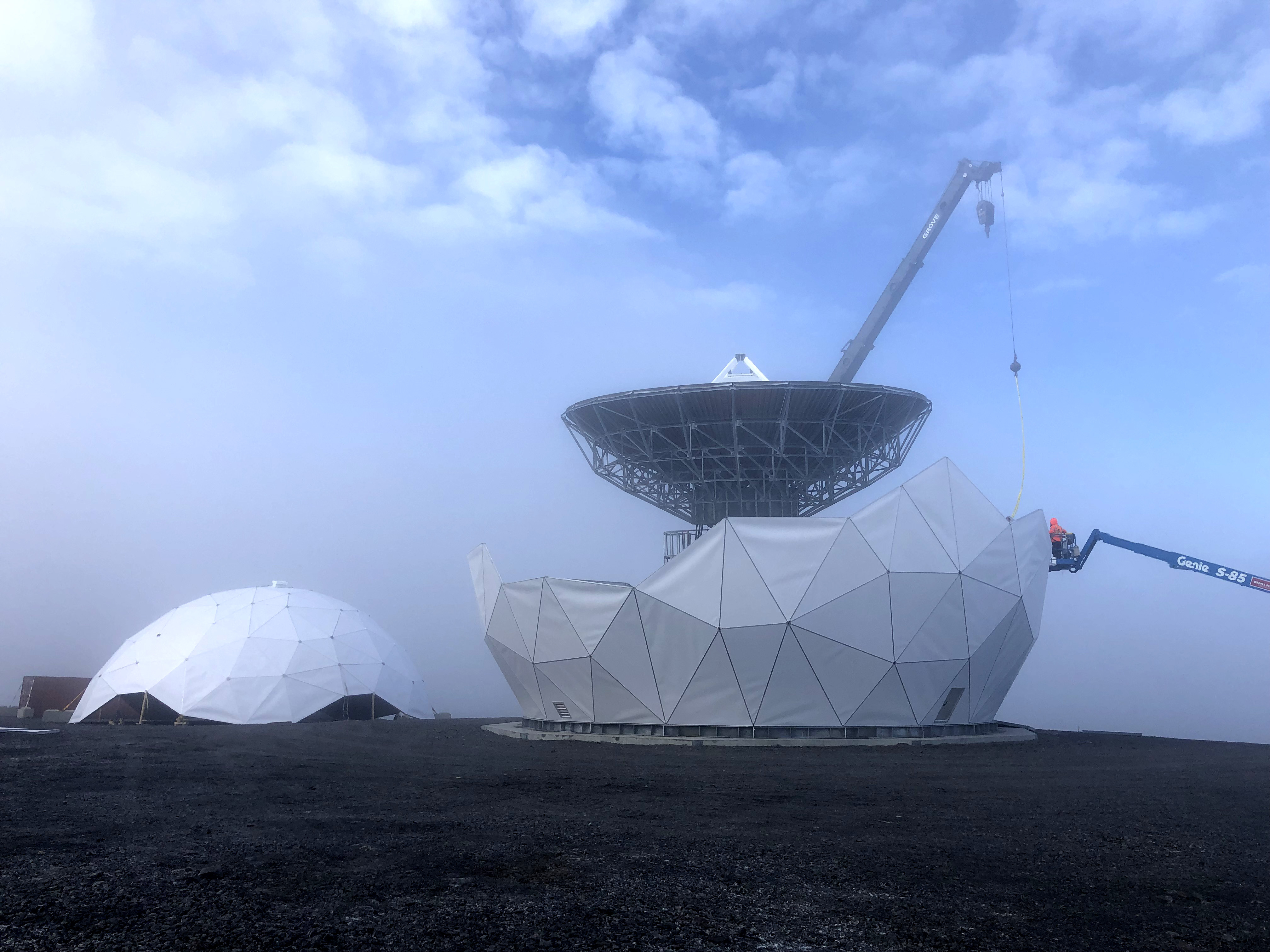 Construction workers build a geodesic dome to cover a satellite dish.