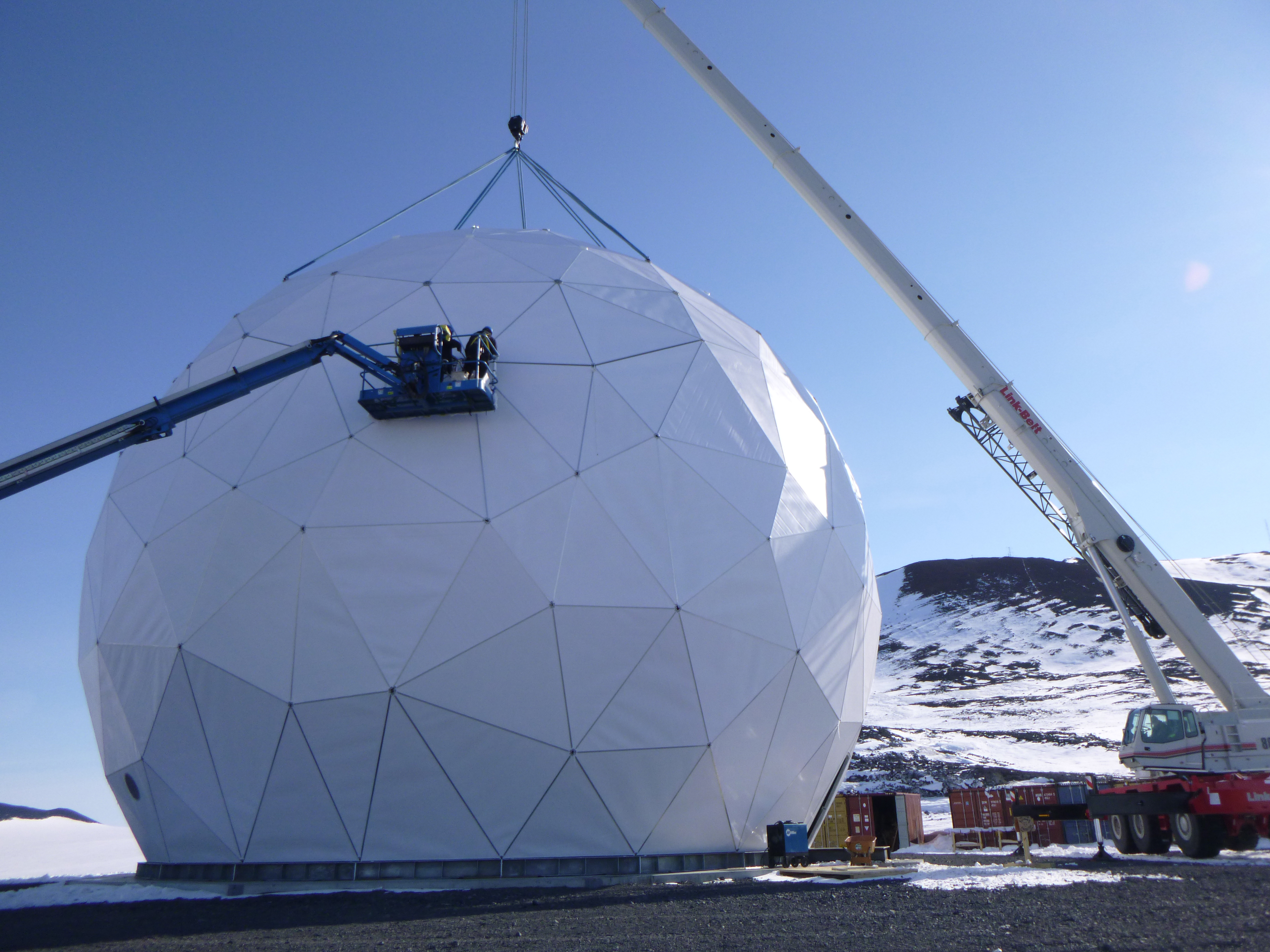 Construction workers in a person-lift working on a geodesic dome.