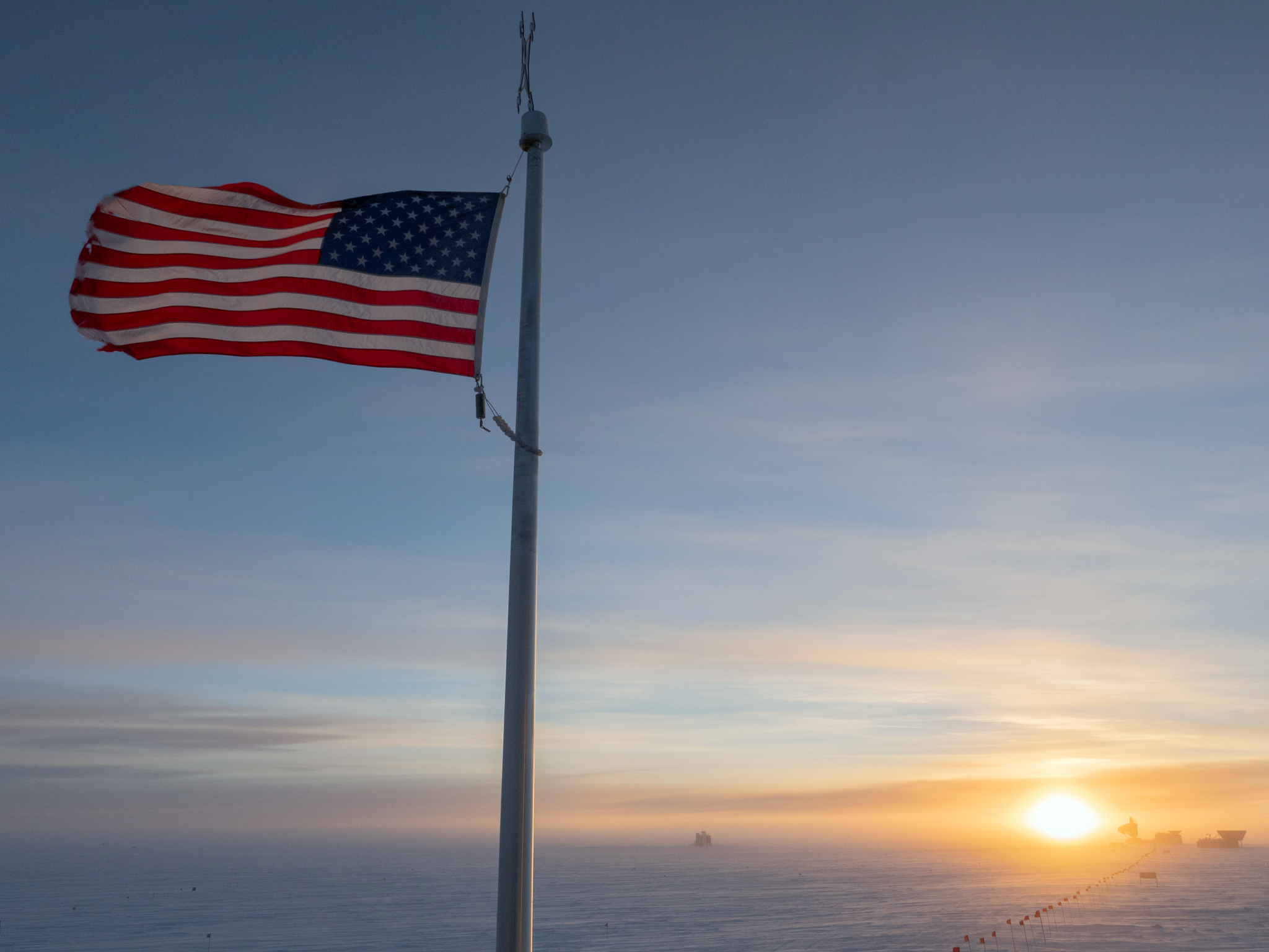 A U.S. flag flies in the foreground, with a sunset on the horizon.