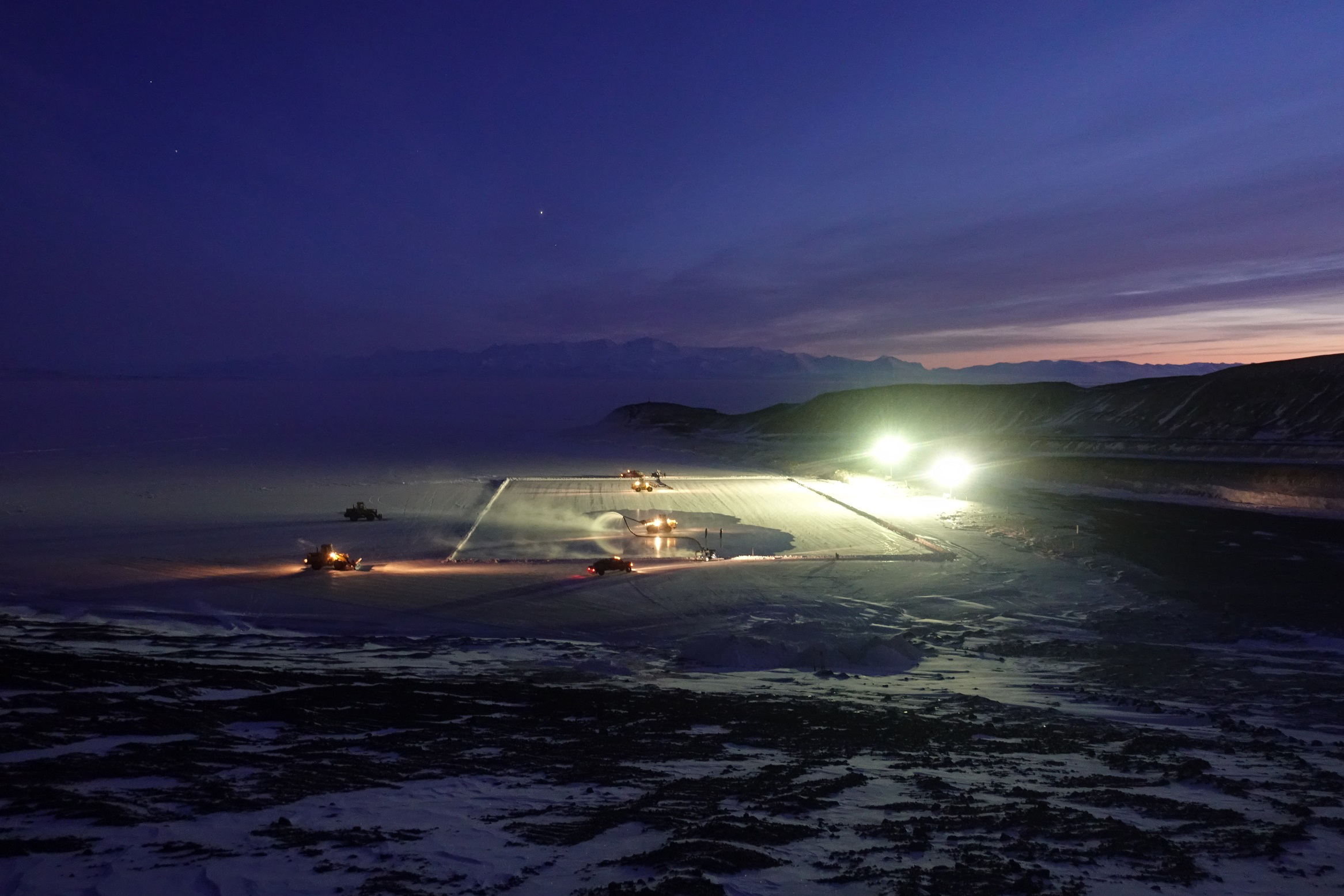 Tractors grooming ice under bright lights at night.