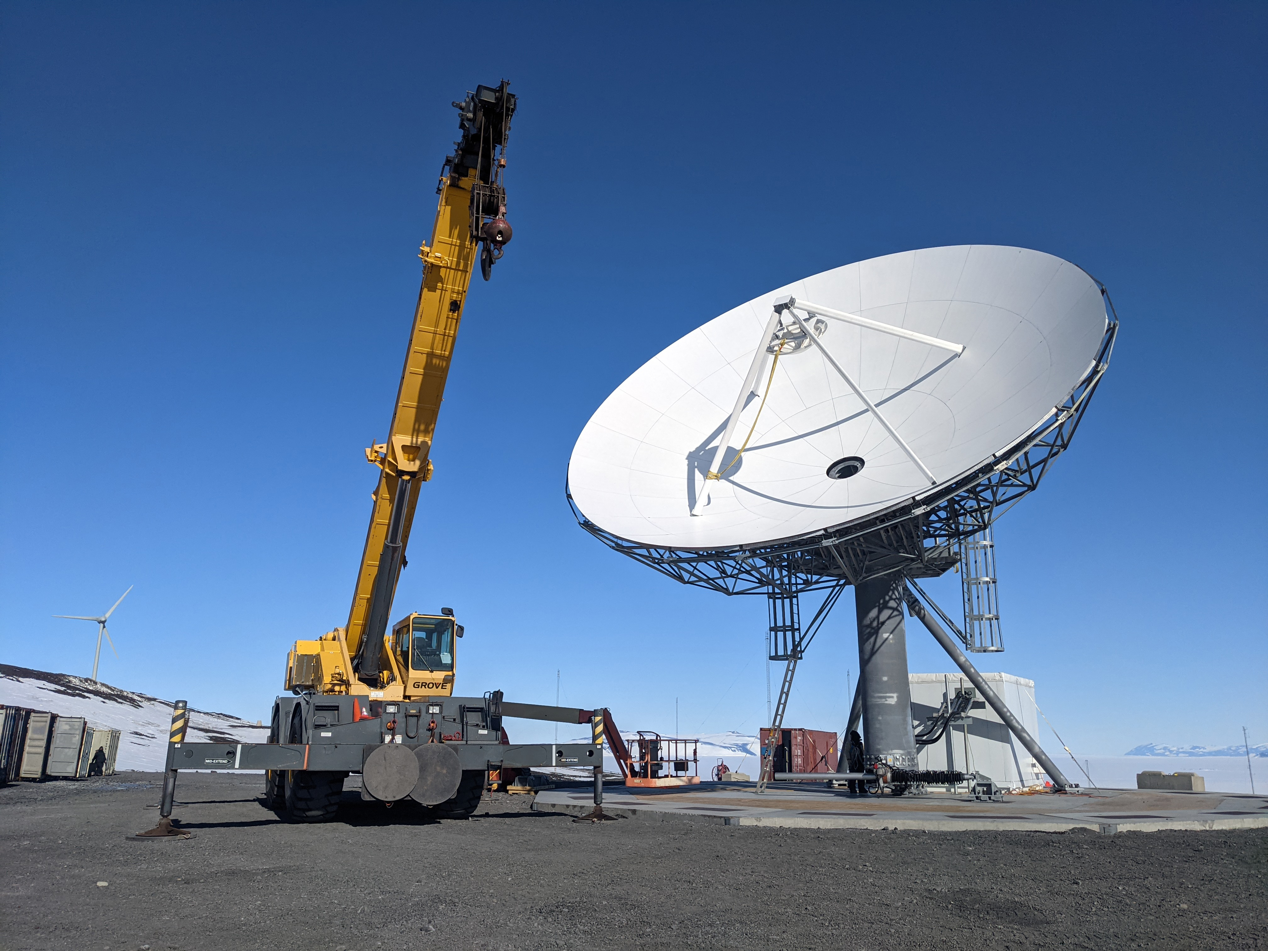 A crane next to a communications satellite dish.