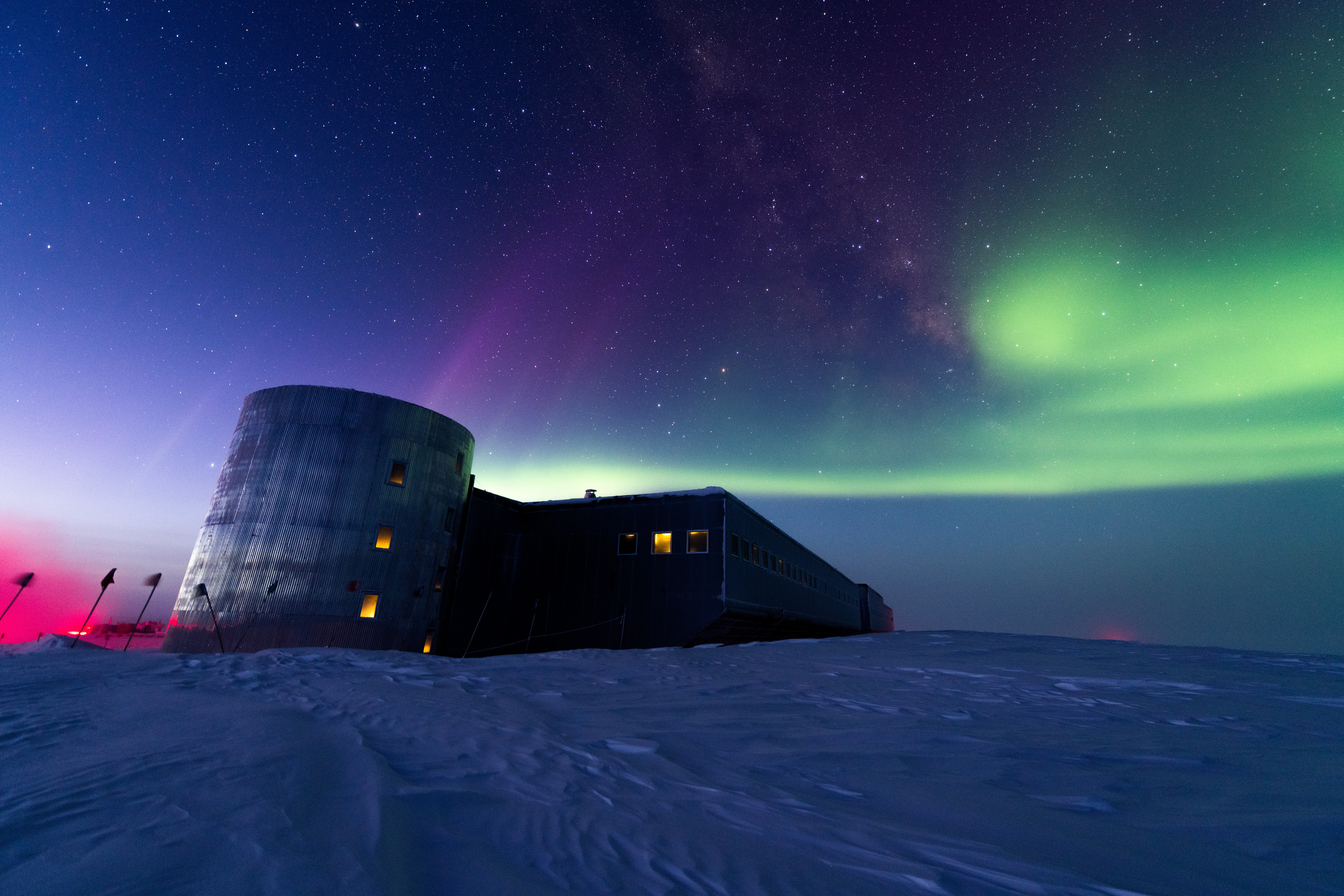 an icy landscape, a building, and green auroras in the night sky. 
