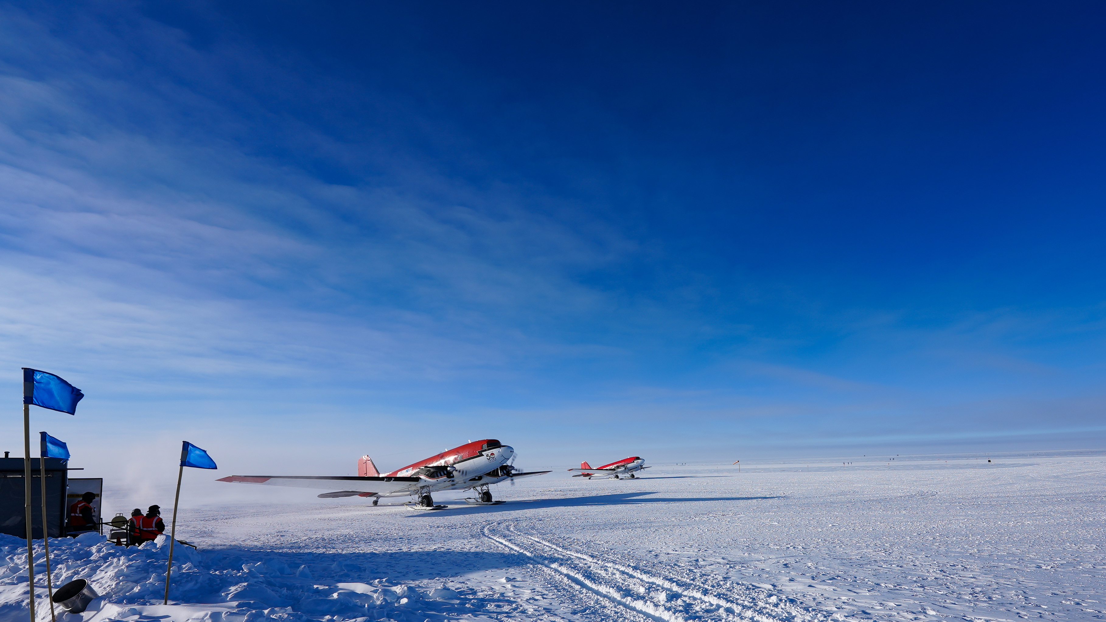 Two red and white airplanes with skis prepare to take off from a snow-covered landscape.