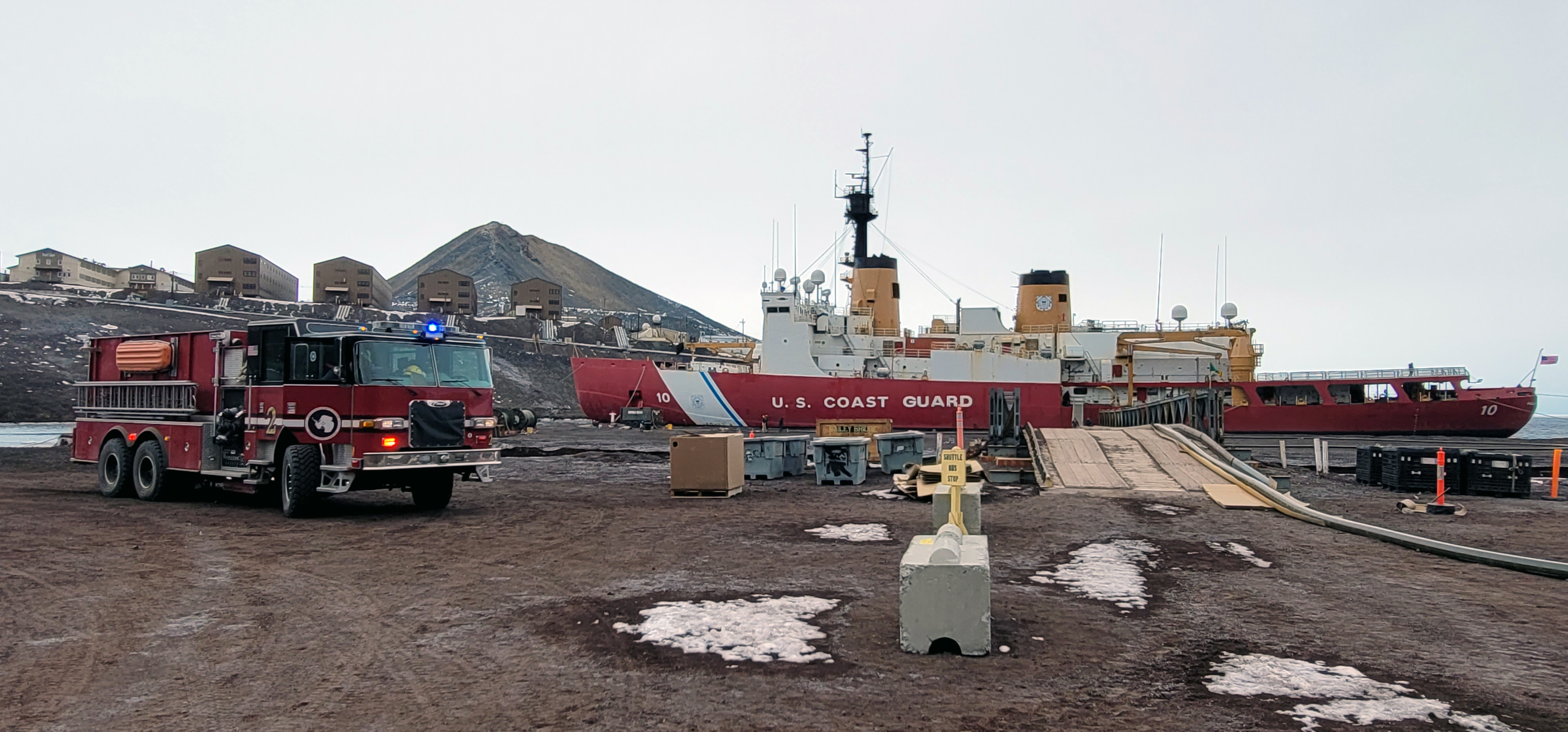 A fire truck is parked near a Coast Guard ship tied to a pier.