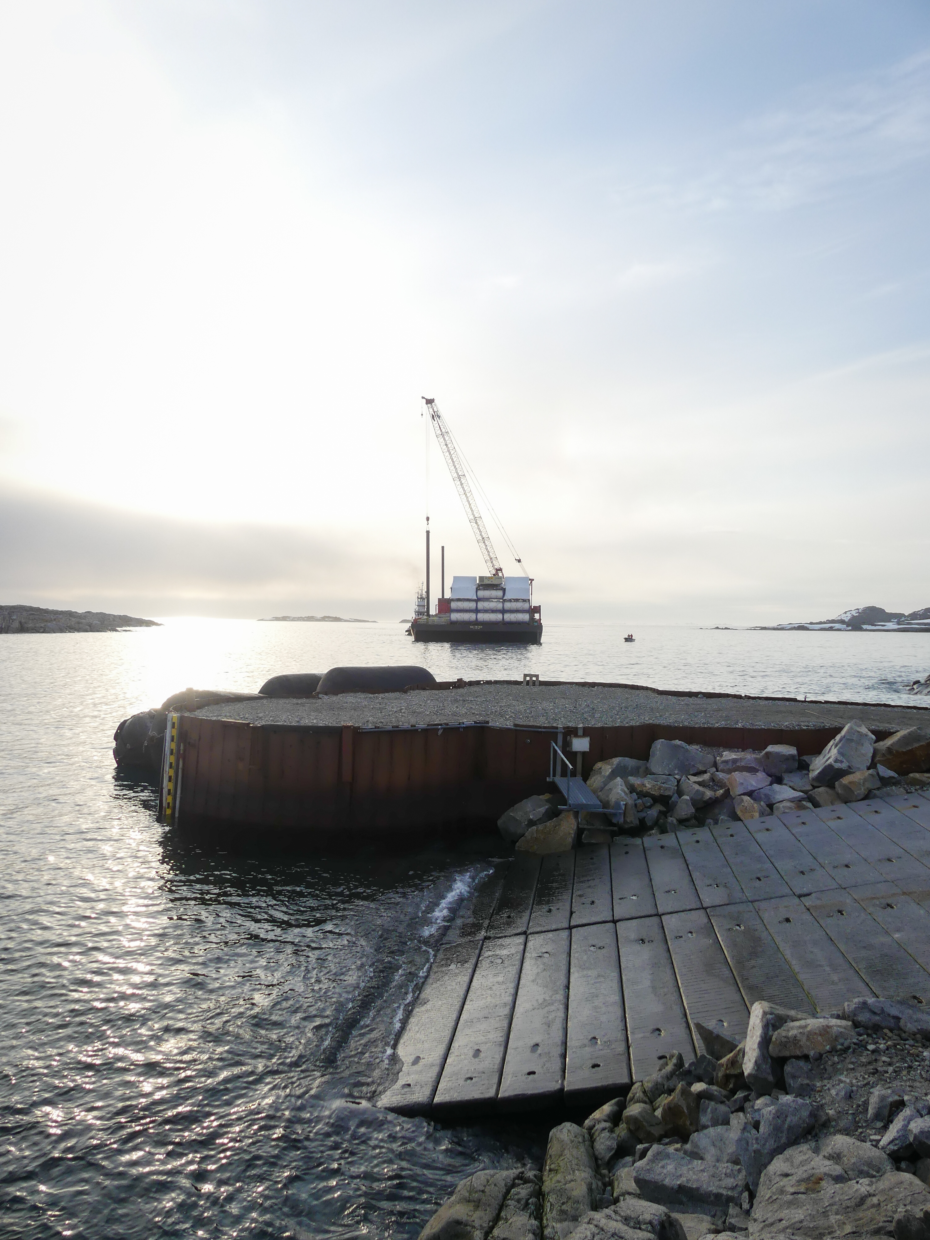 A barge and crane in the background behind a flat pier. 