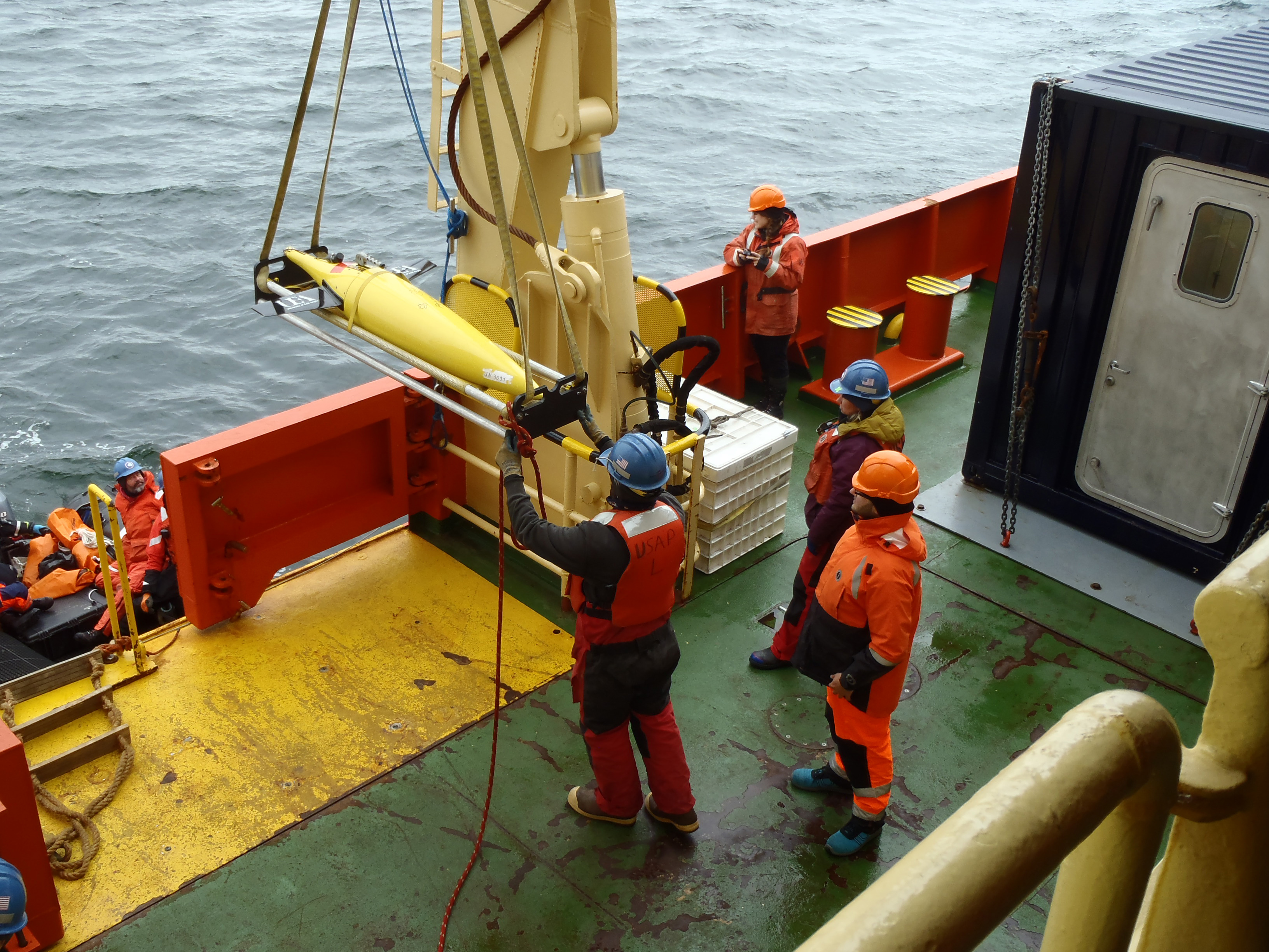 Marine personnel deploying an autonomous ocean glider off the deck of a ship.