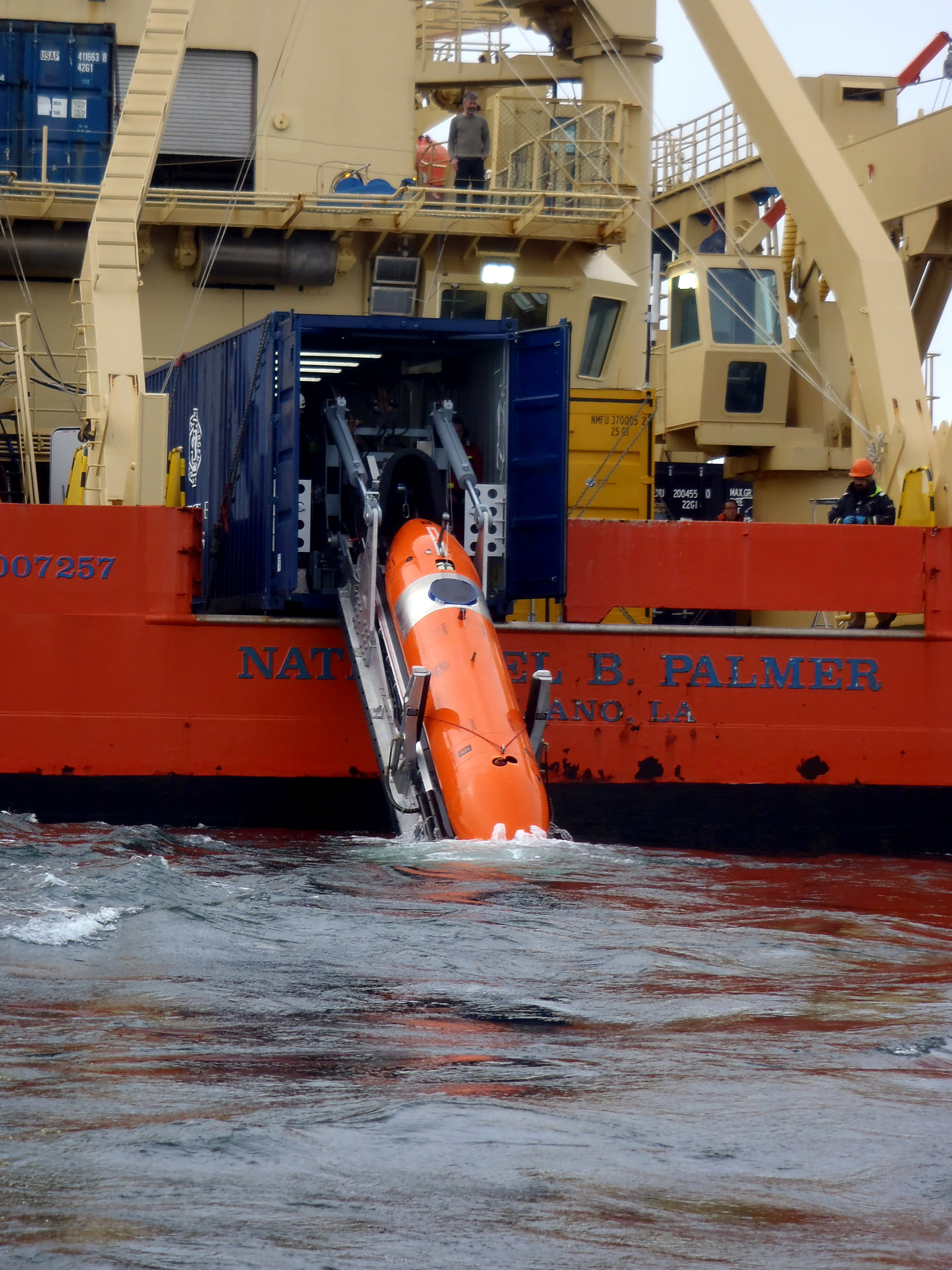 An orange underwater vehicle is deployed off the deck of a ship.