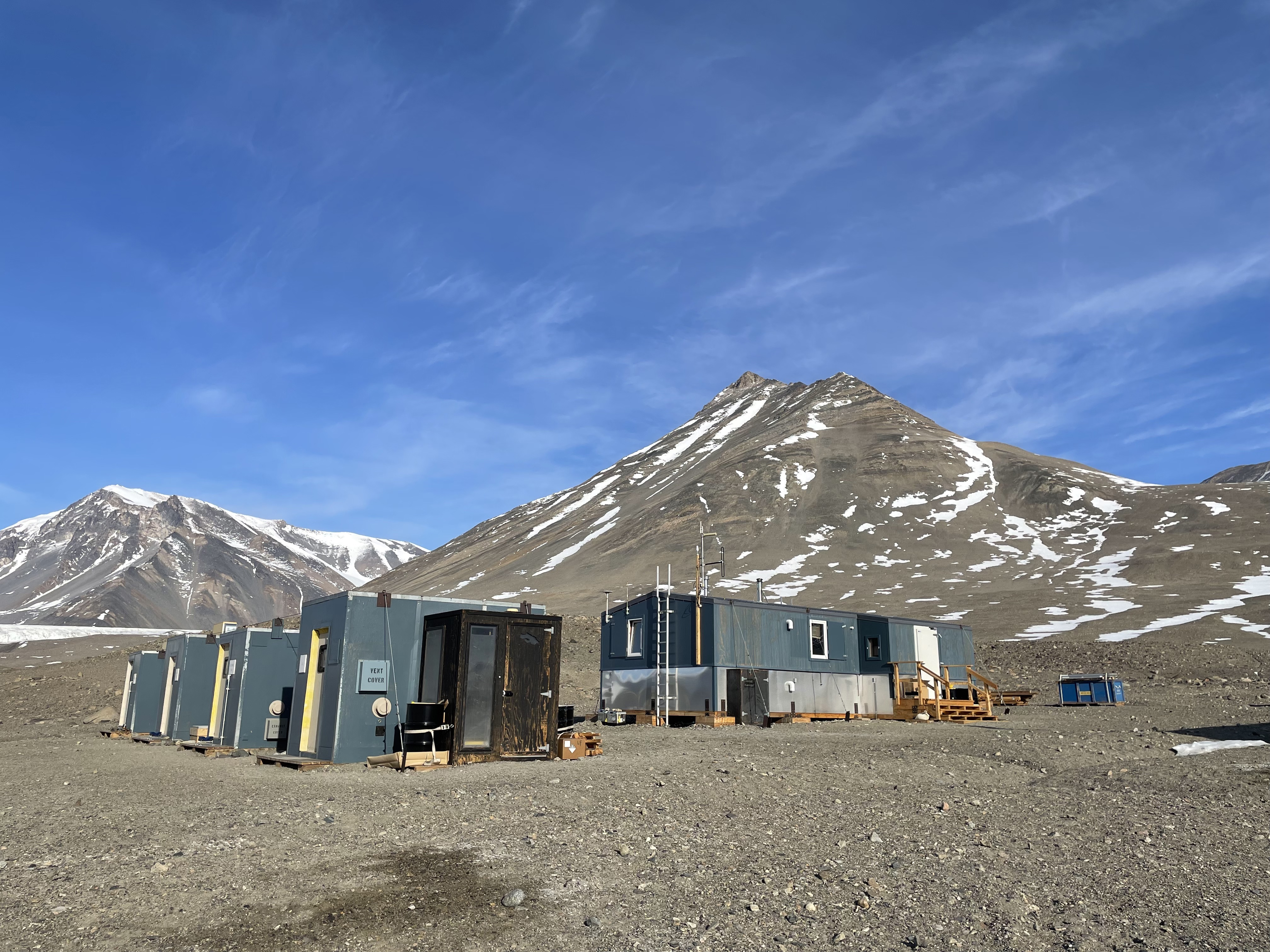 Several small blue wooden buildings in a rocky valley.