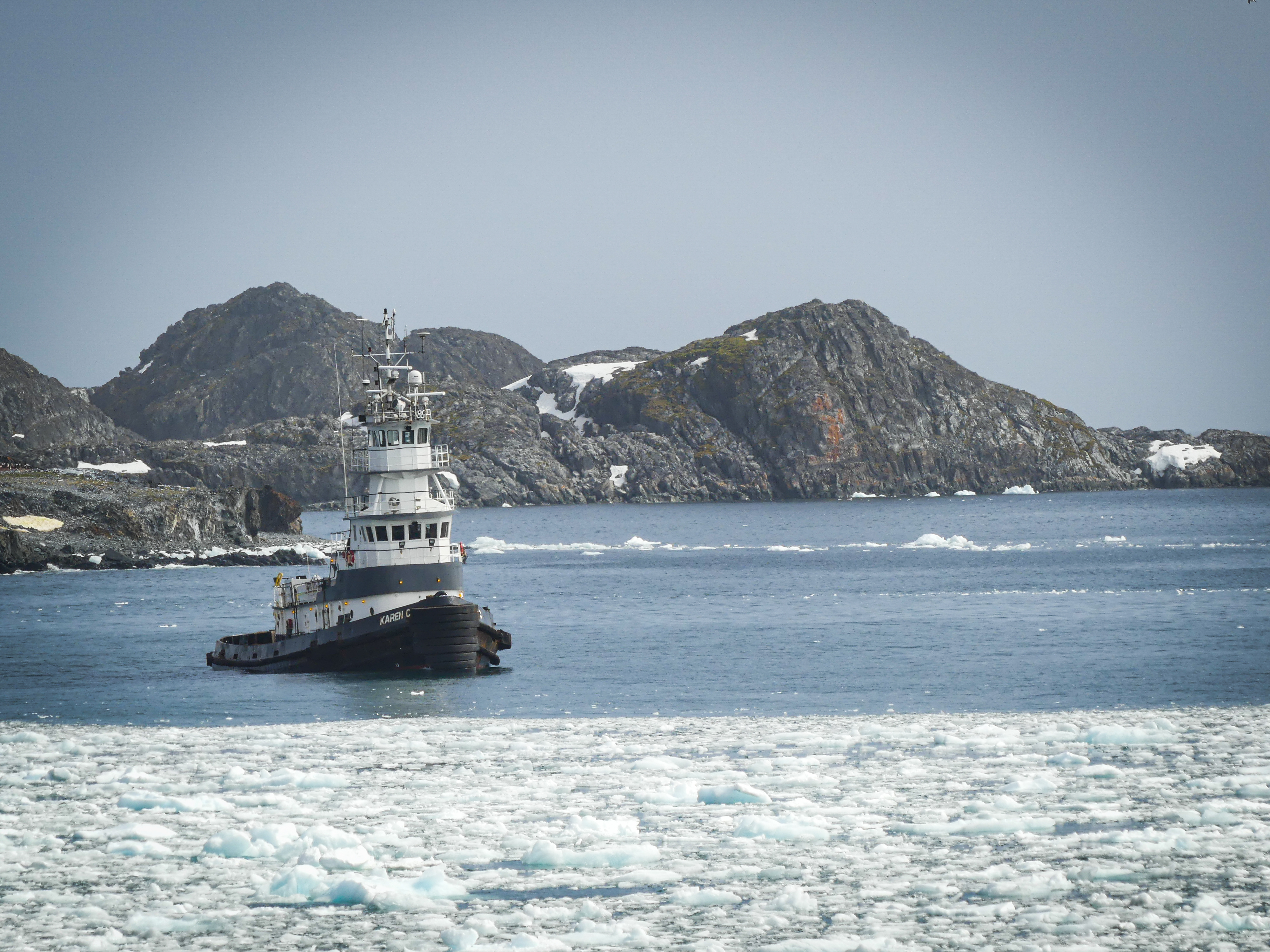 A tugboat in icy water with mountains behind it. 