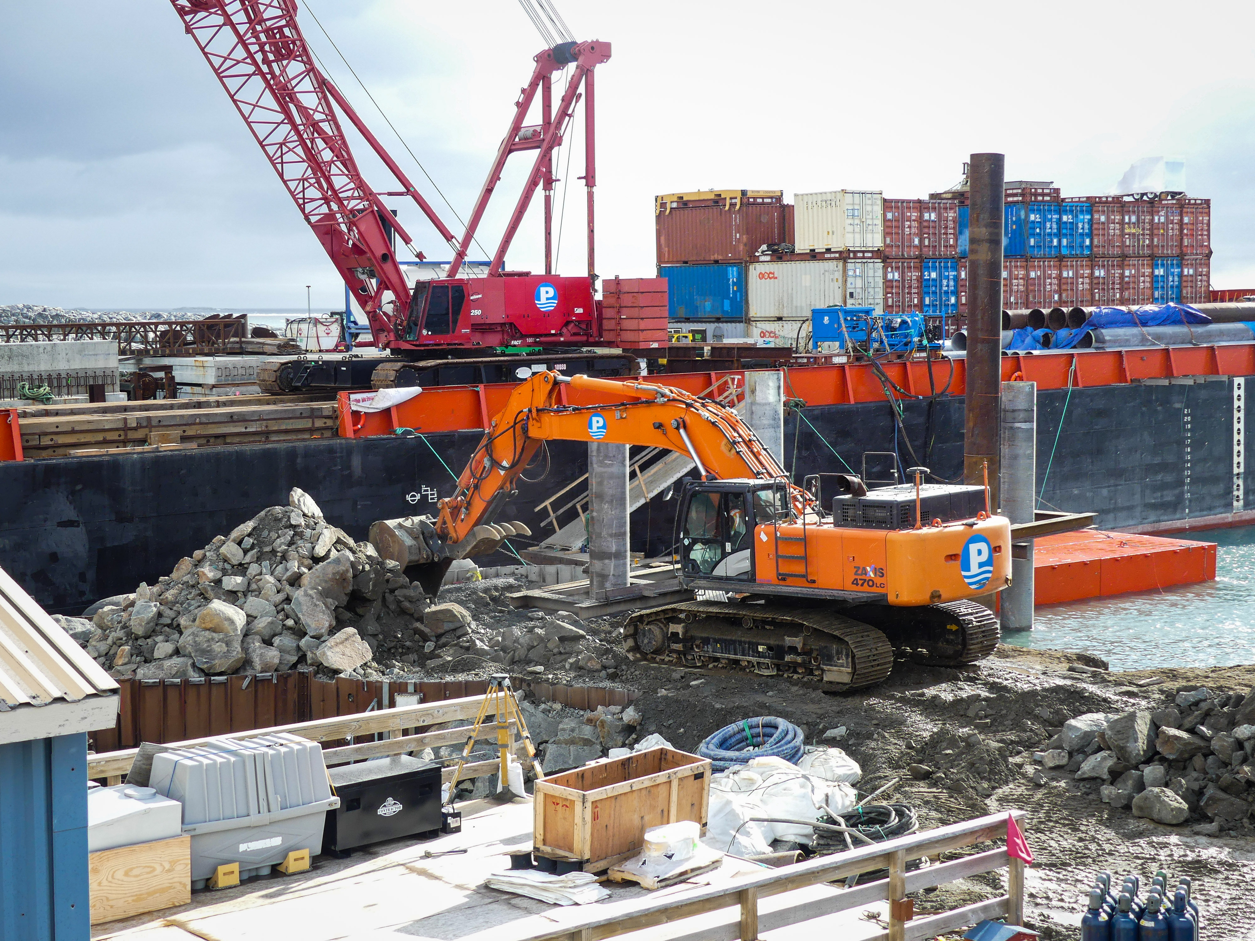 A backhoe clears away rubble consisting of large rocks. 