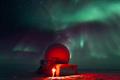 an icy landscape, a radome structure, and green auroras in the night sky. 