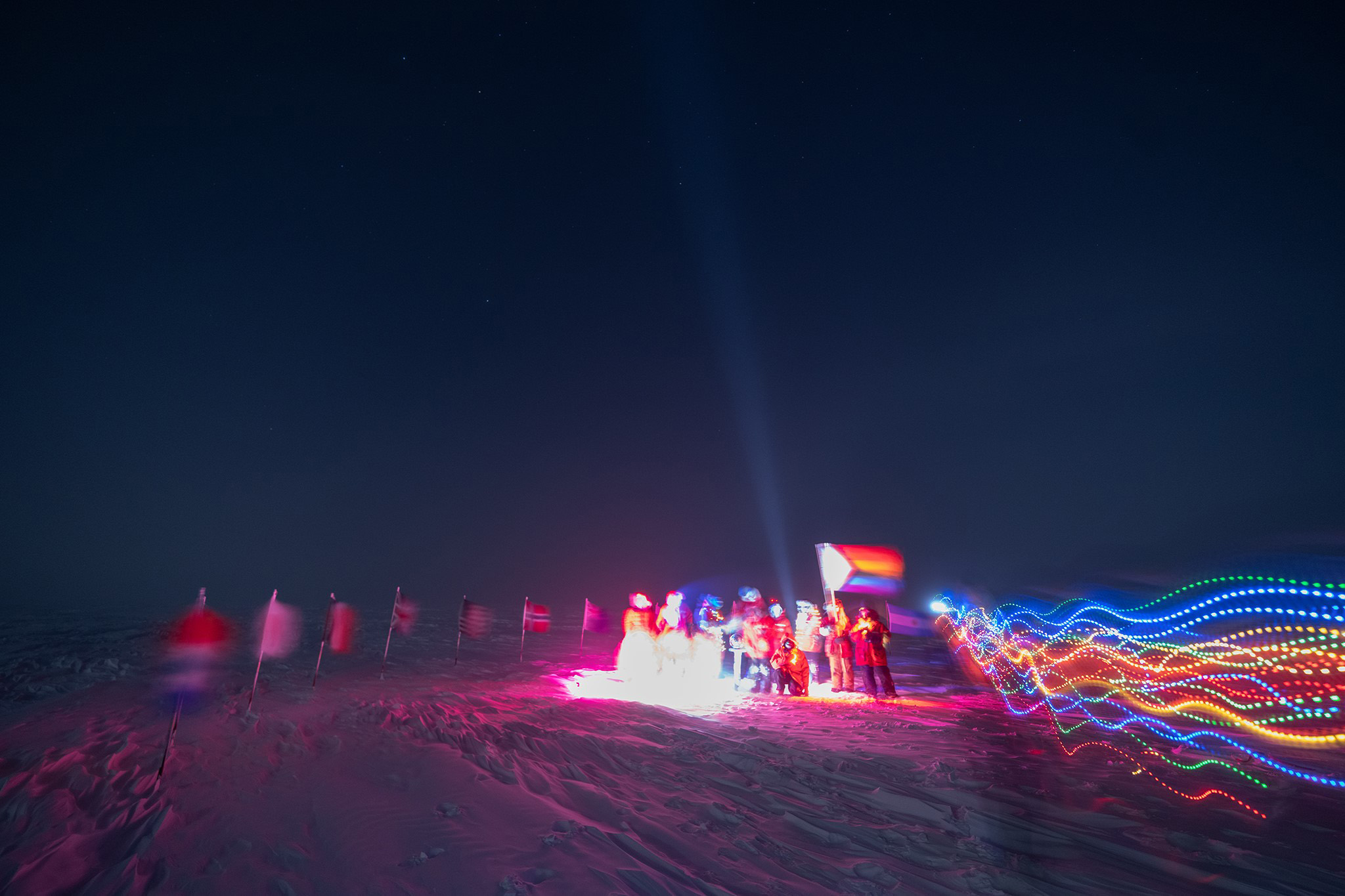 A group holds a Pride flag at the ceremonial Pole in the dark of winter.